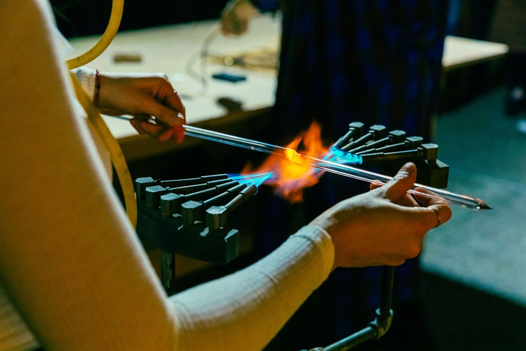 A person is bending a glass tube in a custom neon burner, with a flame directed at the glass.