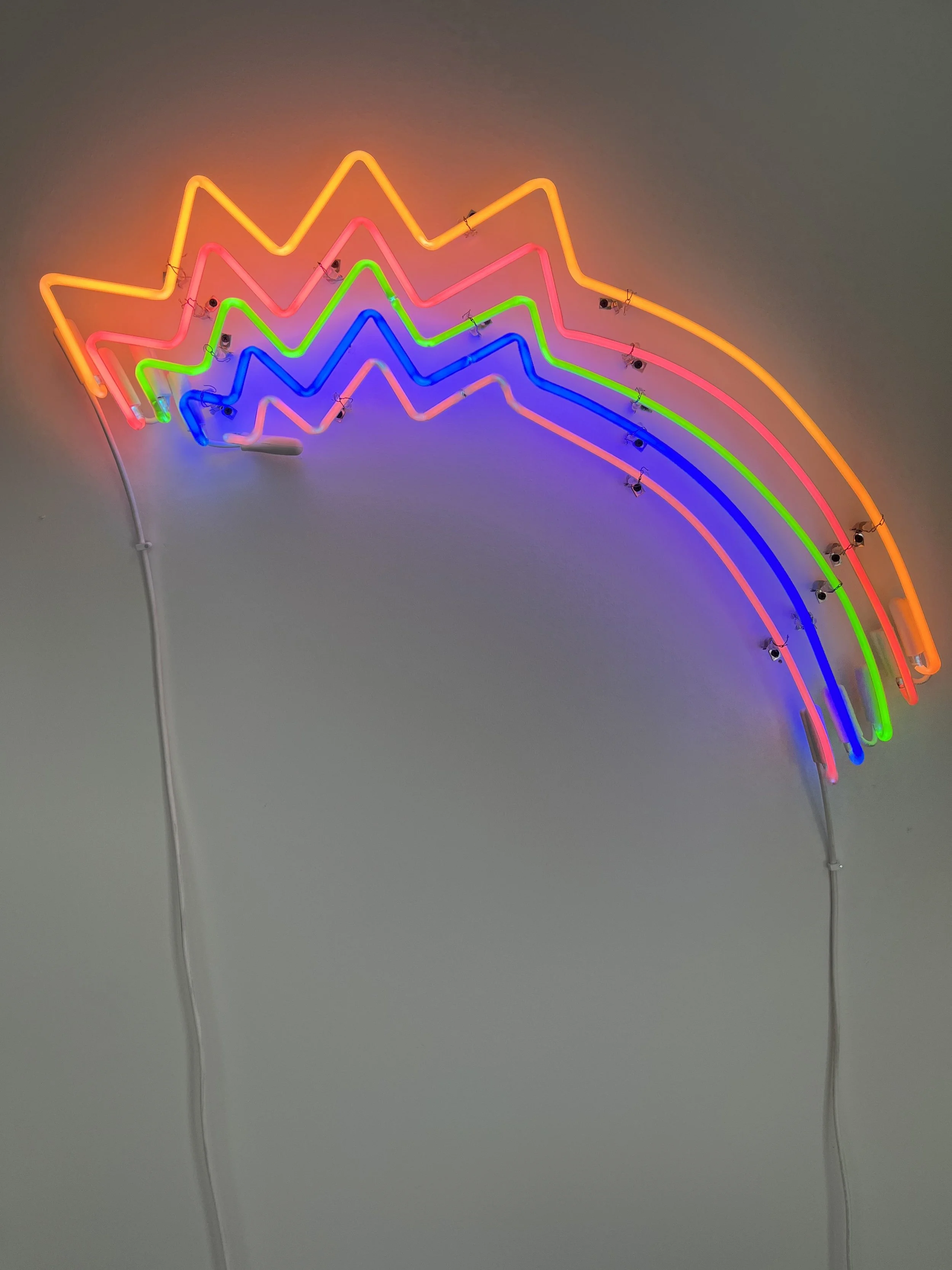 Colorful neon sign with rainbow shape on a plain wall.