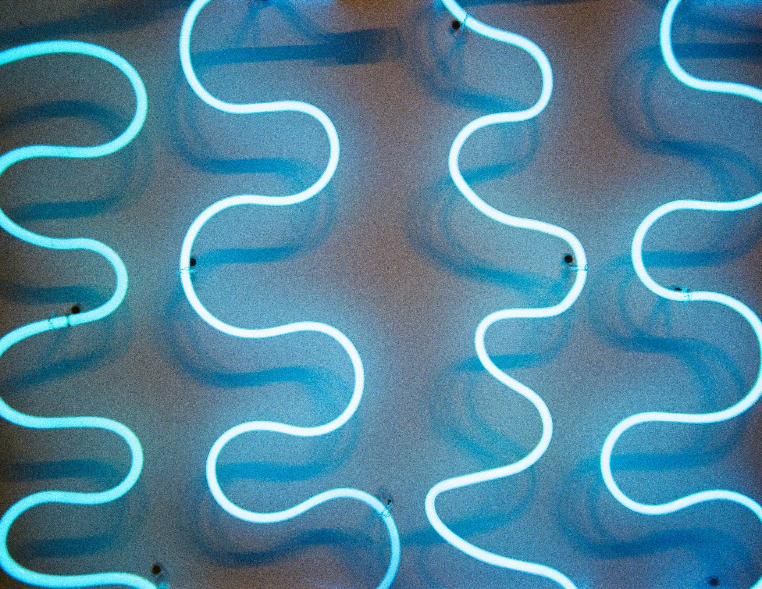 Multiple blue neon wavy lines on a wall creating a pattern.