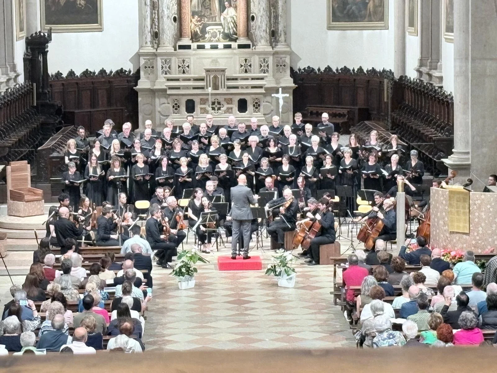 Choir and orchestra performing inside a church or cathedral with an audience watching.