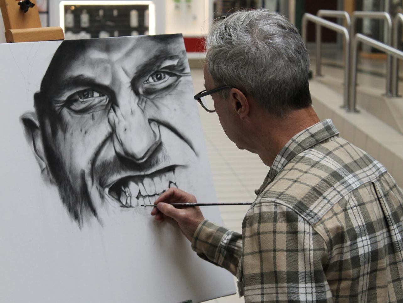 Un artiste peint un portrait en noir et blanc d'une personne âgée avec des traits détaillés sur une toile.
