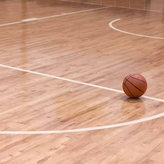 A basketball on a wooden basketball court with white lines.