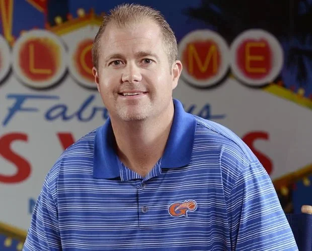 A man in a blue striped polo shirt sitting in front of a colorful sign that reads 'Lowe's Fabul...'