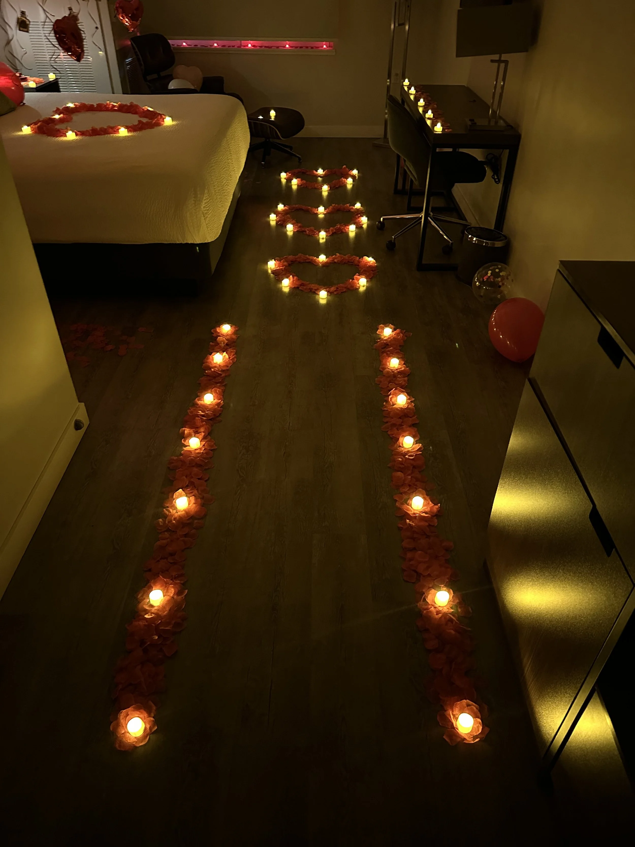 Room decorated with candles and rose petals for Valentine's Day or romantic occasion; candle-lit pathways and hearts on bed and wall