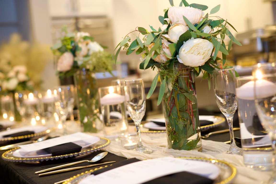 Elegant dining table with floral centerpiece, candles, black and white place settings, and glassware for a special event.