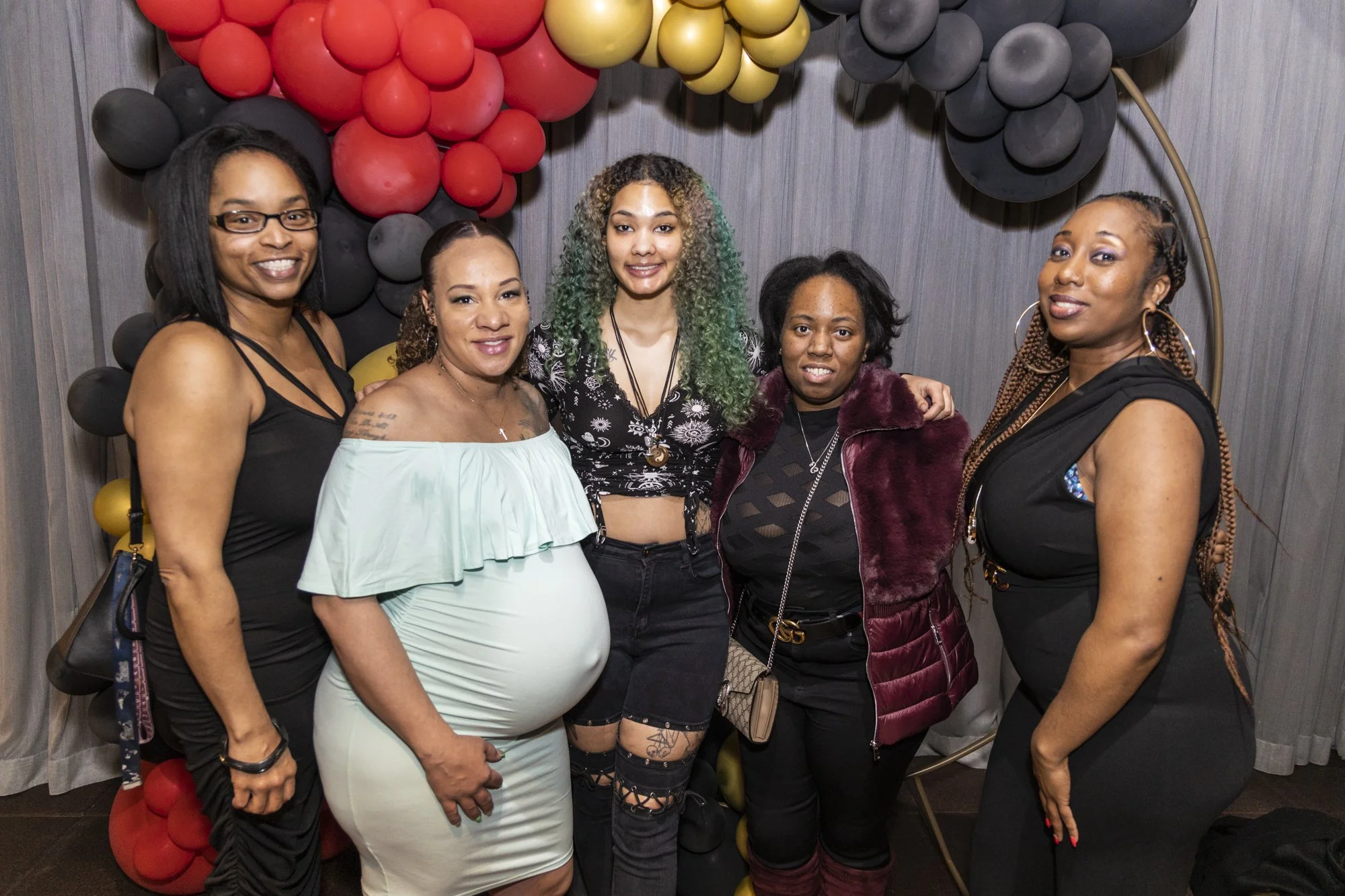 Group of five women standing together in front of a balloon backdrop, smiling at the camera.