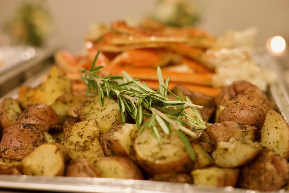 Roasted potatoes garnished with rosemary with a side of crab cakes and crab legs in the background.