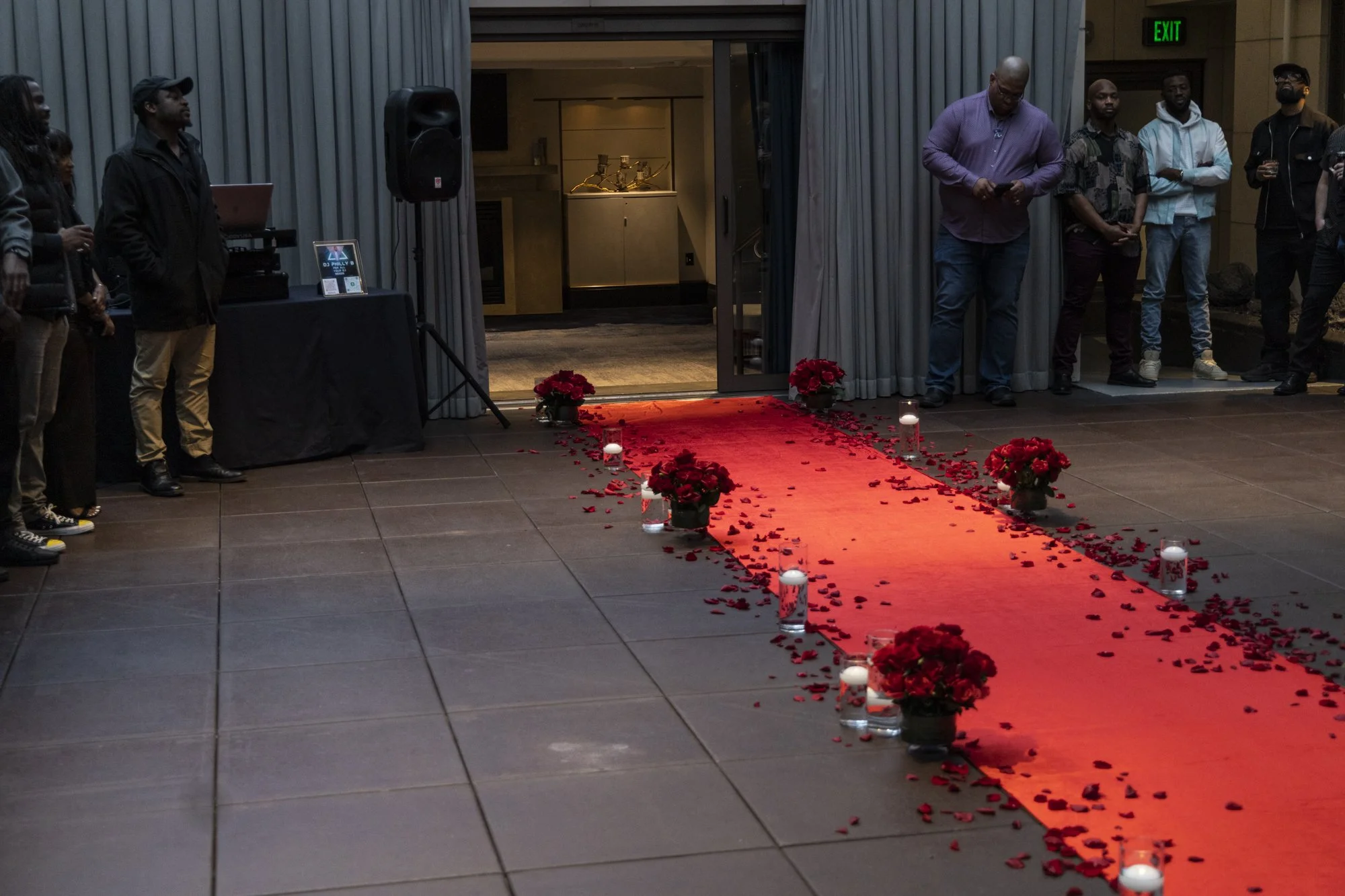 People gathered around a red carpet leading into a room for a memorial or tribute with flowers and candles
