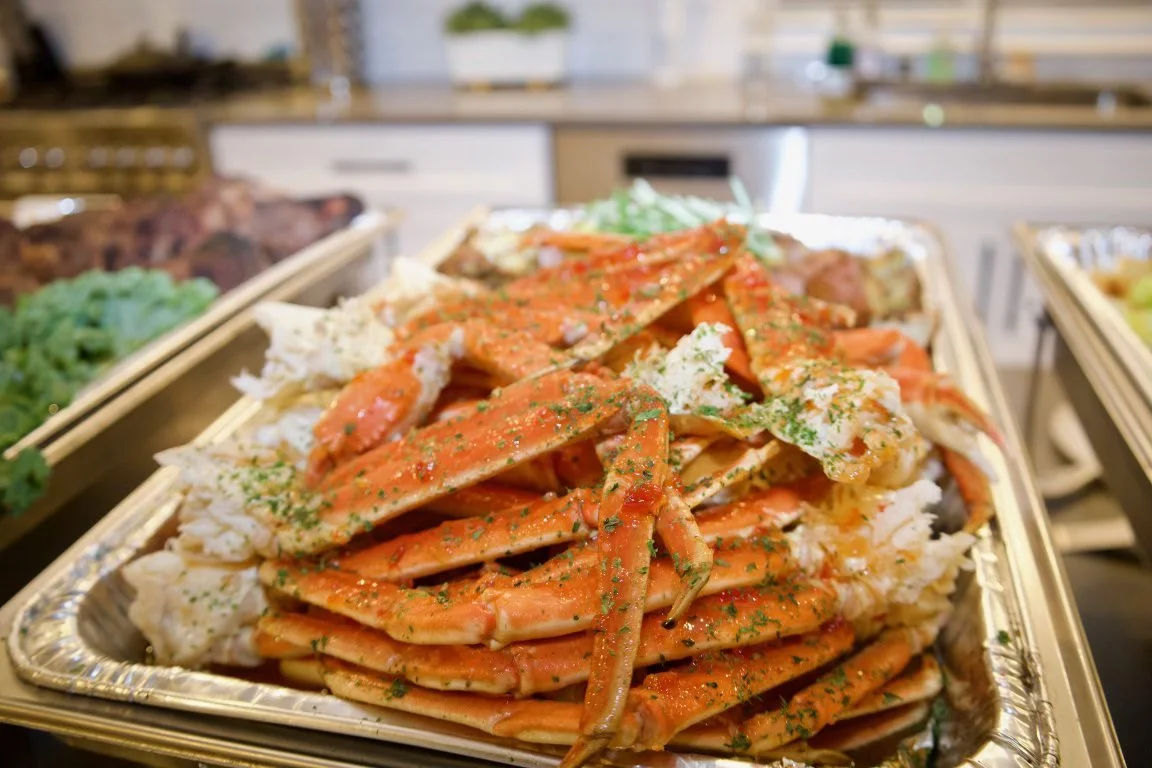 Large aluminum tray filled with cooked crab legs garnished with herbs, displayed on a buffet table.
