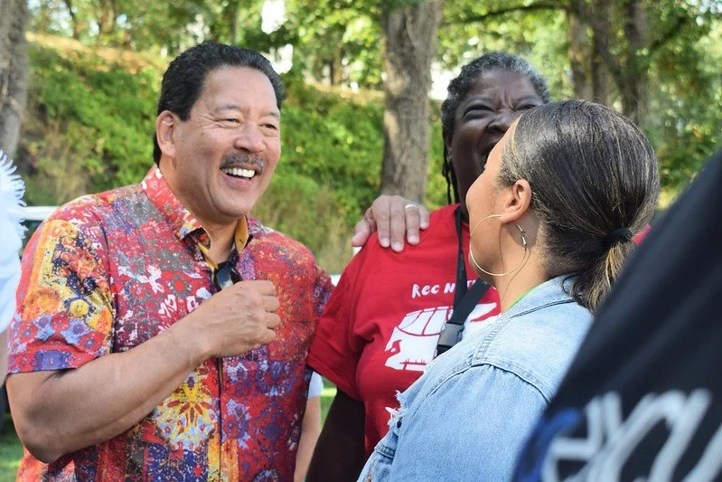 Three people, two women and a man, are outdoors and smiling or laughing while having a conversation.