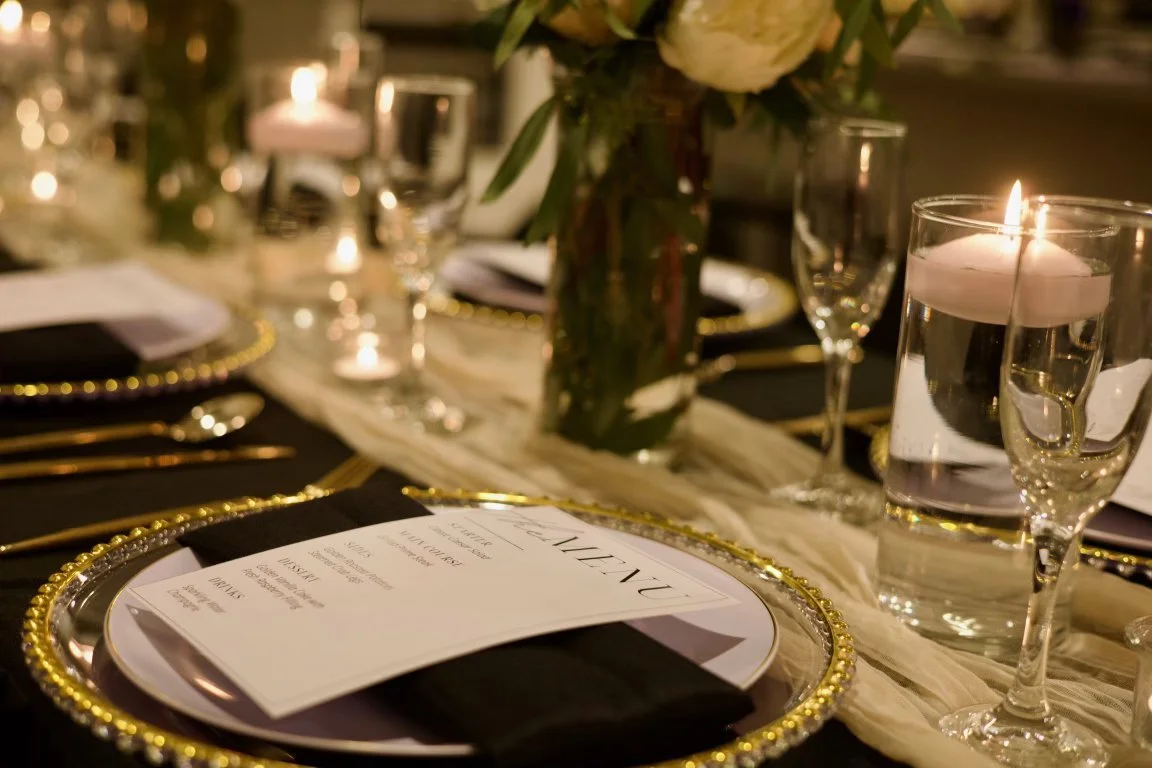 Elegant table setting with candlelight, floral centerpiece, menu, and glassware for a formal event.