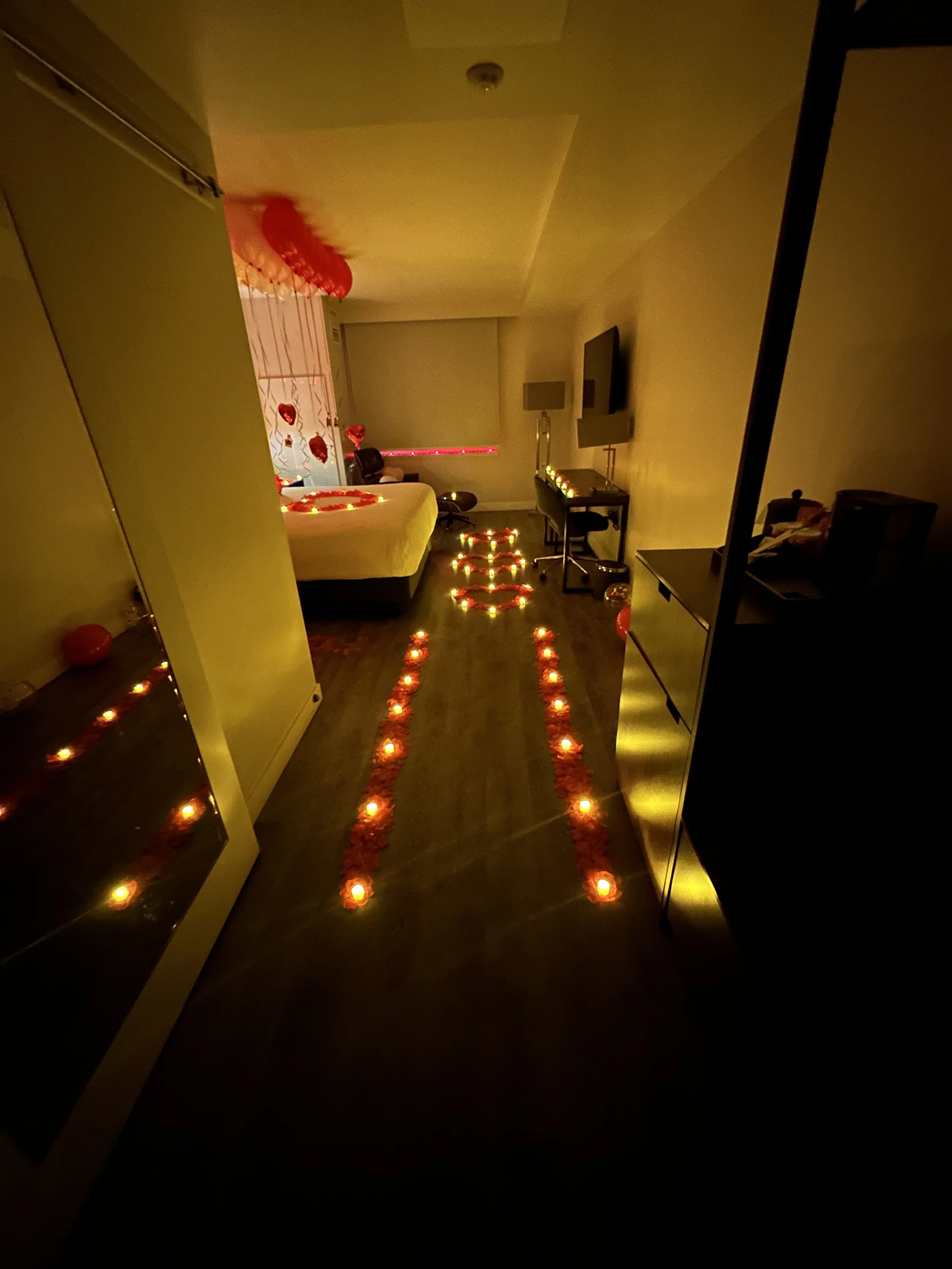 Hotel room decorated with red candles, balloons, and heart-shaped decorations for a romantic occasion.