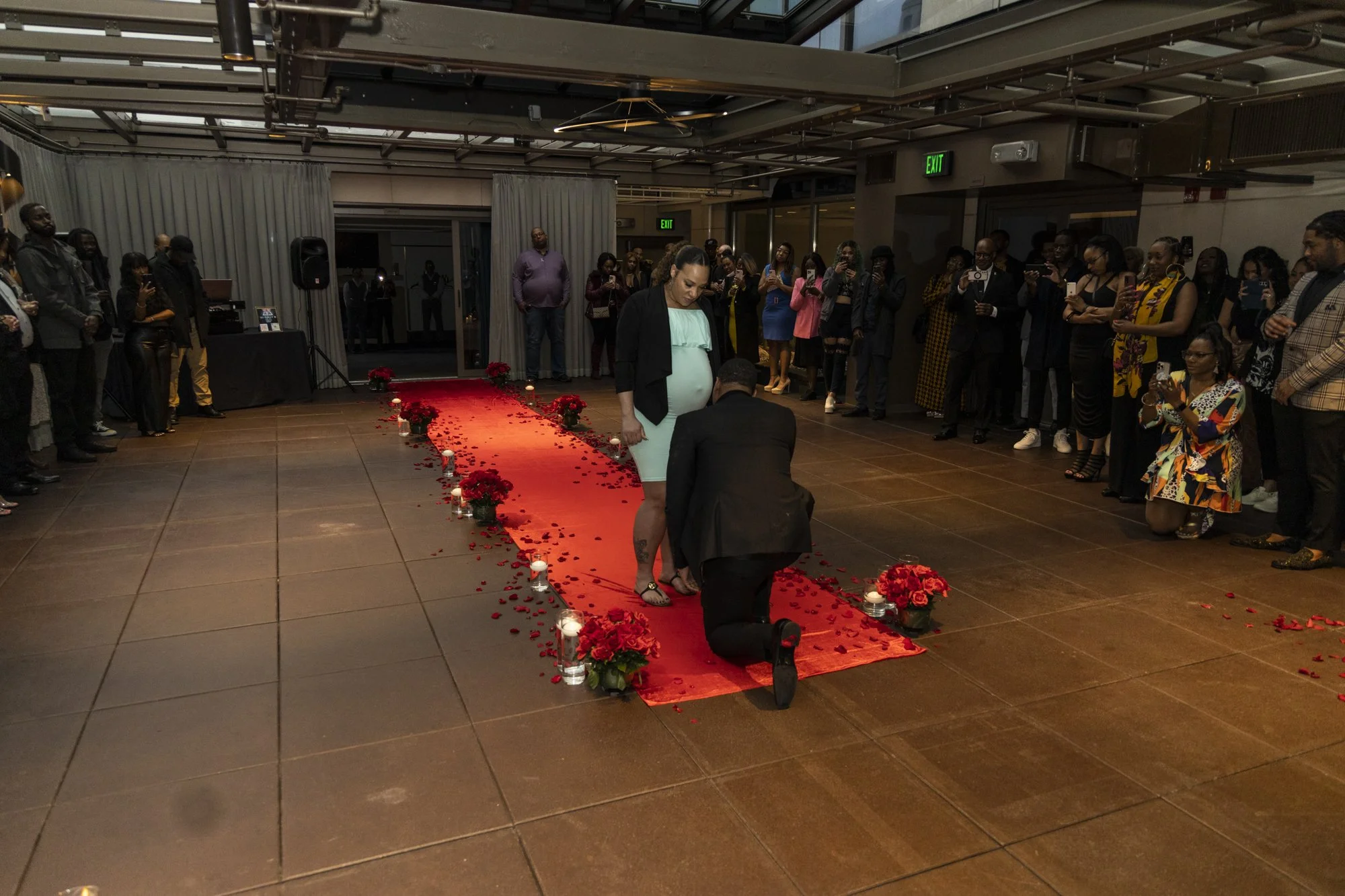 A couple exchanging wedding vows on a red carpet aisle decorated with red flowers and candles, with guests gathered around in a dimly lit indoor venue.