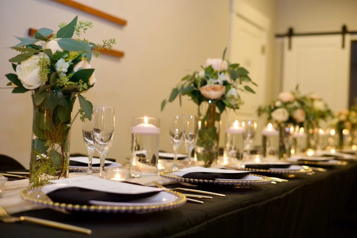 A beautifully decorated banquet table with floral centerpieces, candles, and elegant tableware for a special event or wedding reception.