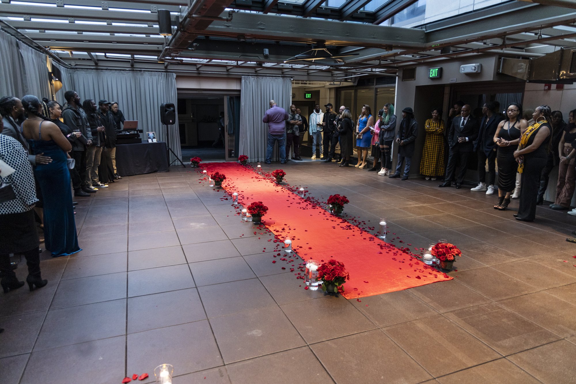Indoor wedding reception with a red carpet aisle decorated with red roses and candles, guests lined up on both sides.