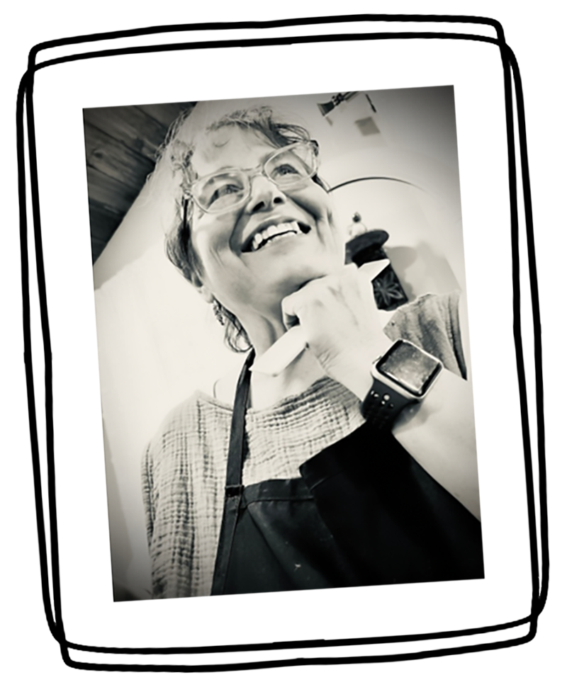 Black and white photo of an older woman with glasses, smiling, holding a phone to her ear, wearing a watch and an apron.