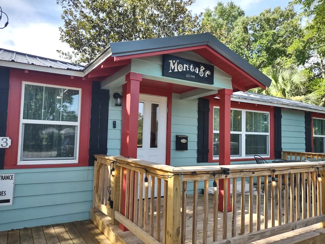 Colorful building with light blue and red exterior, black accents, and a small porch with string lights. The sign reads "Montage – EST 1999" and there are trees in the background.