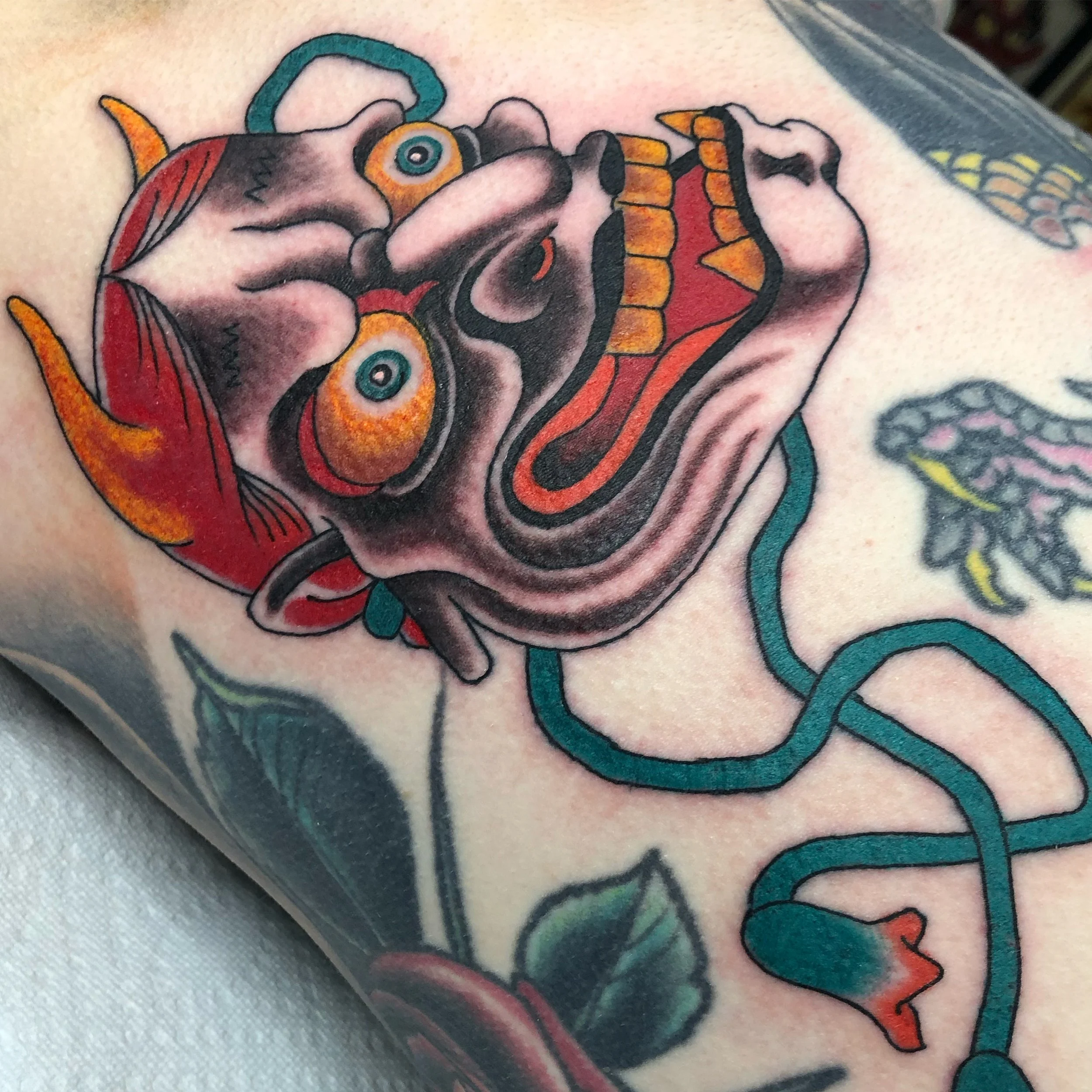 Colorful traditional tattoo of a Hannya mask, and a coiled line on skin.