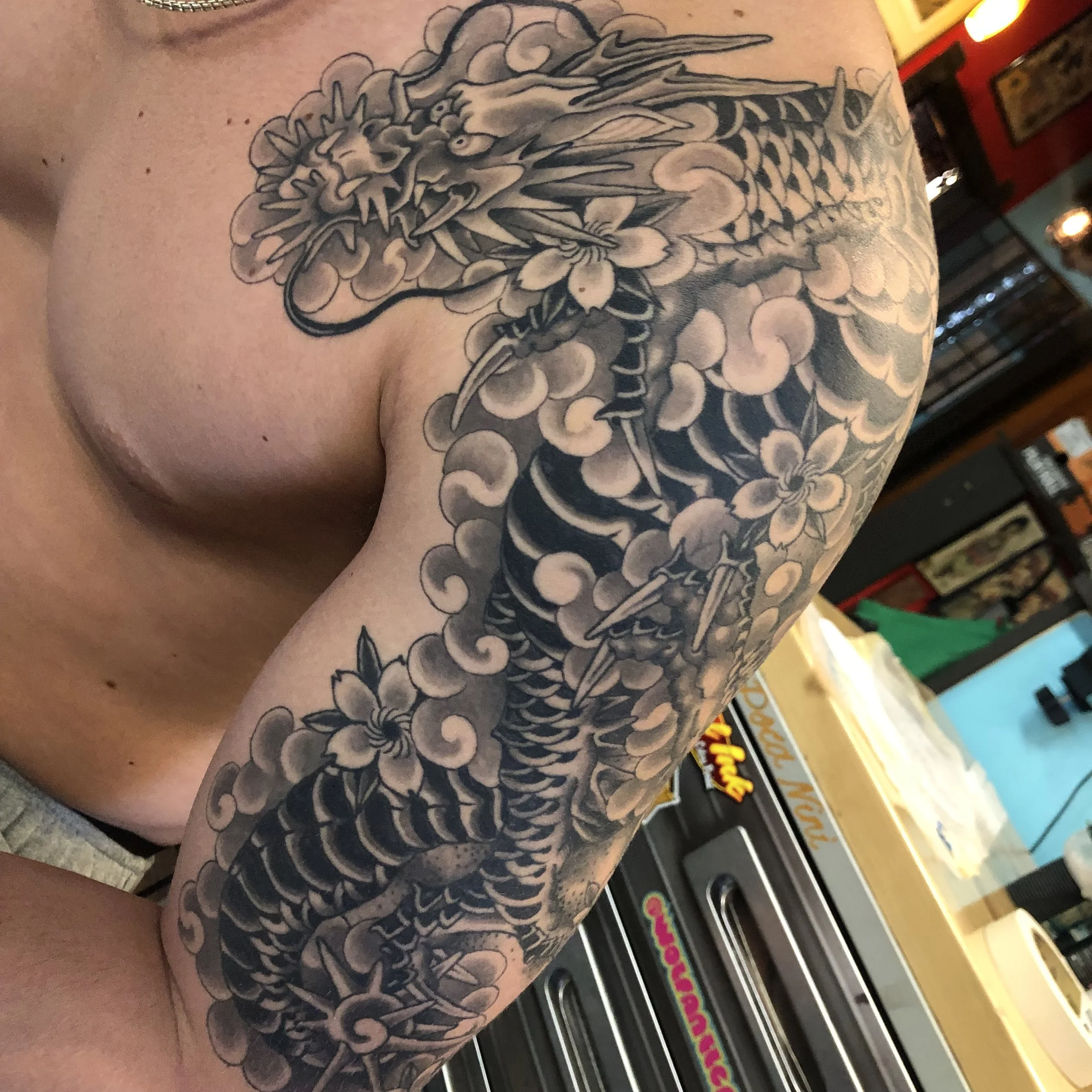 Black and gray tattoo of a dragon intertwined with cherry blossoms on person's upper arm and shoulder.
