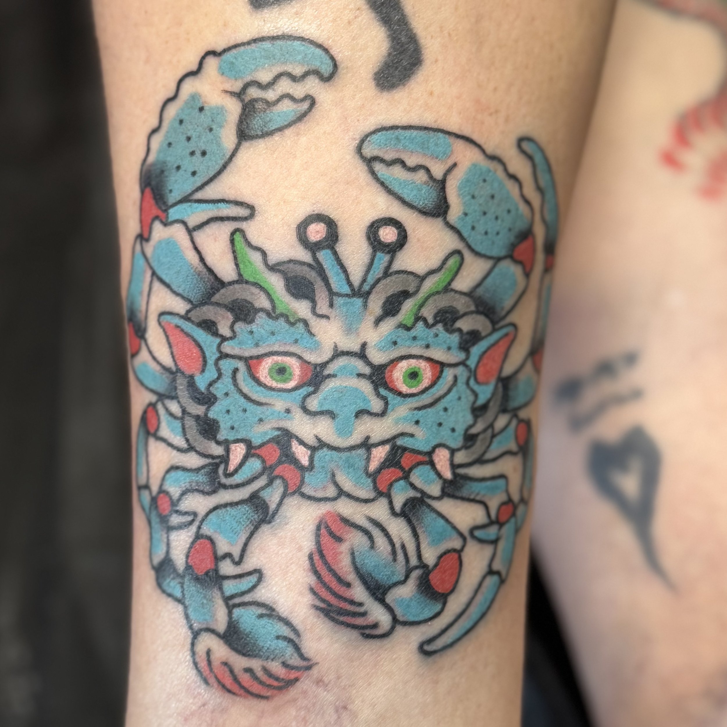 Colorful tattoo of a fierce-looking blue Heike crab with green eyes and prominent claws.
