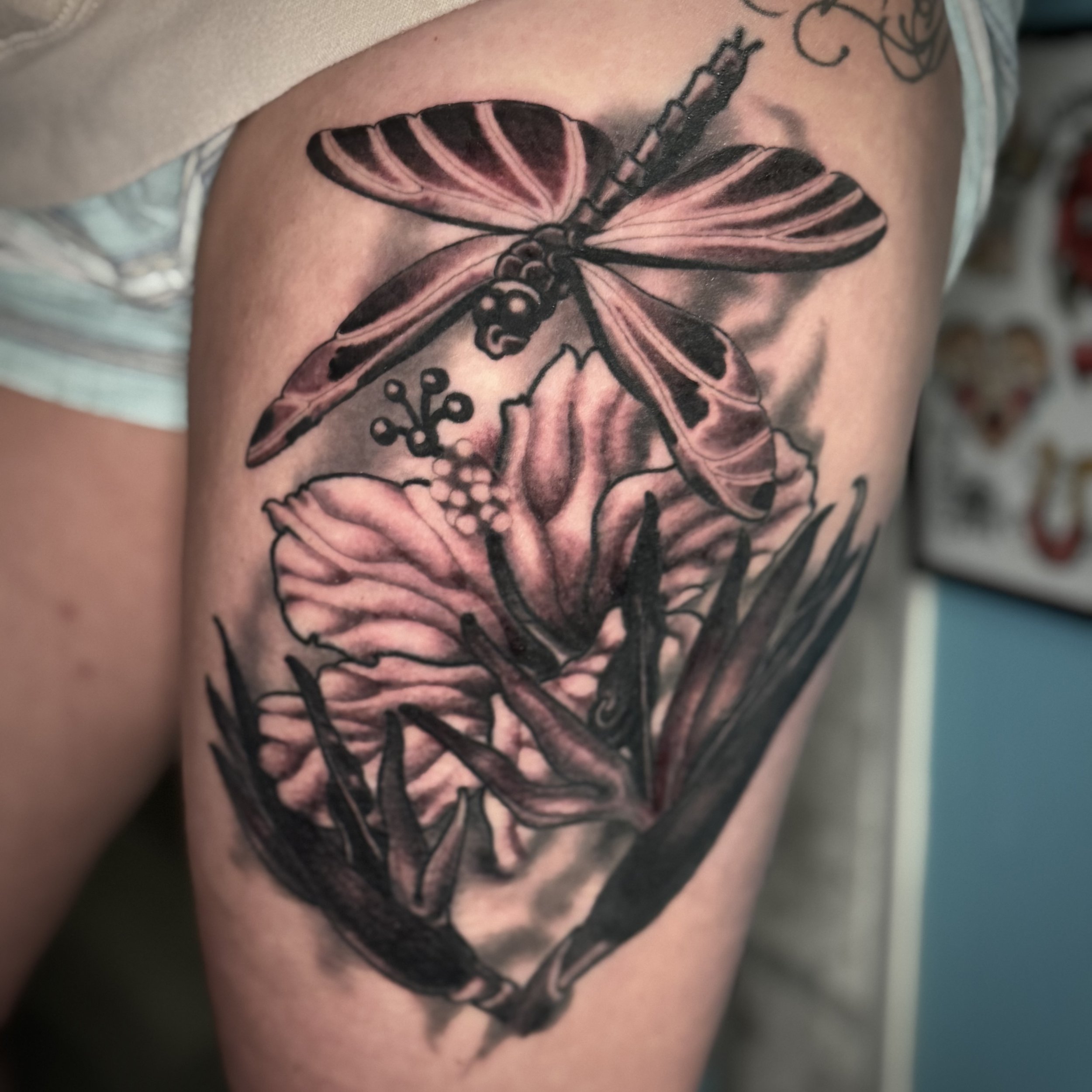 Tattoo of a dragonfly above a flower on a person's upper thigh