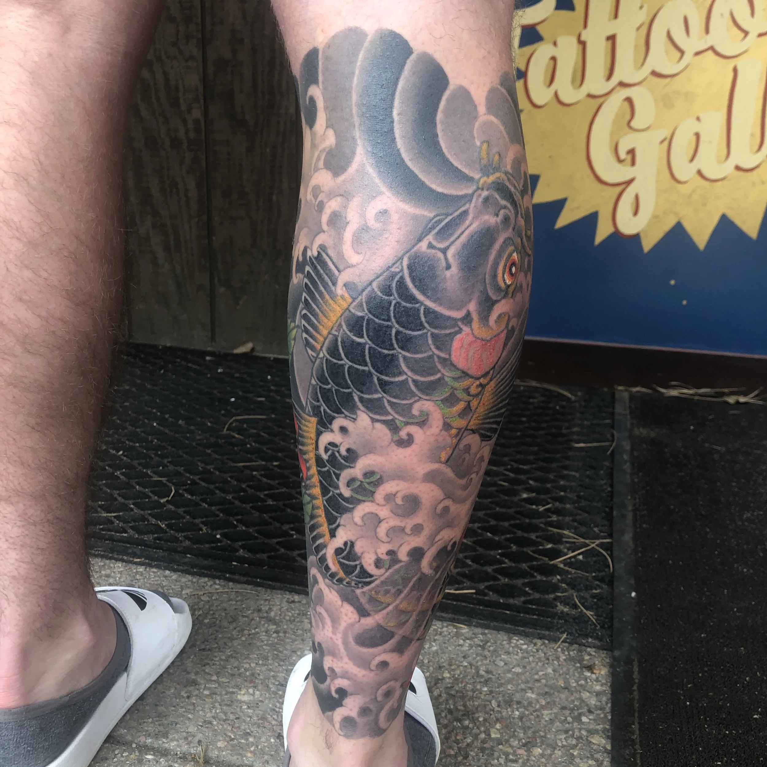 Colorful tattoo of a koi fish with waves and clouds on a person's lower leg.