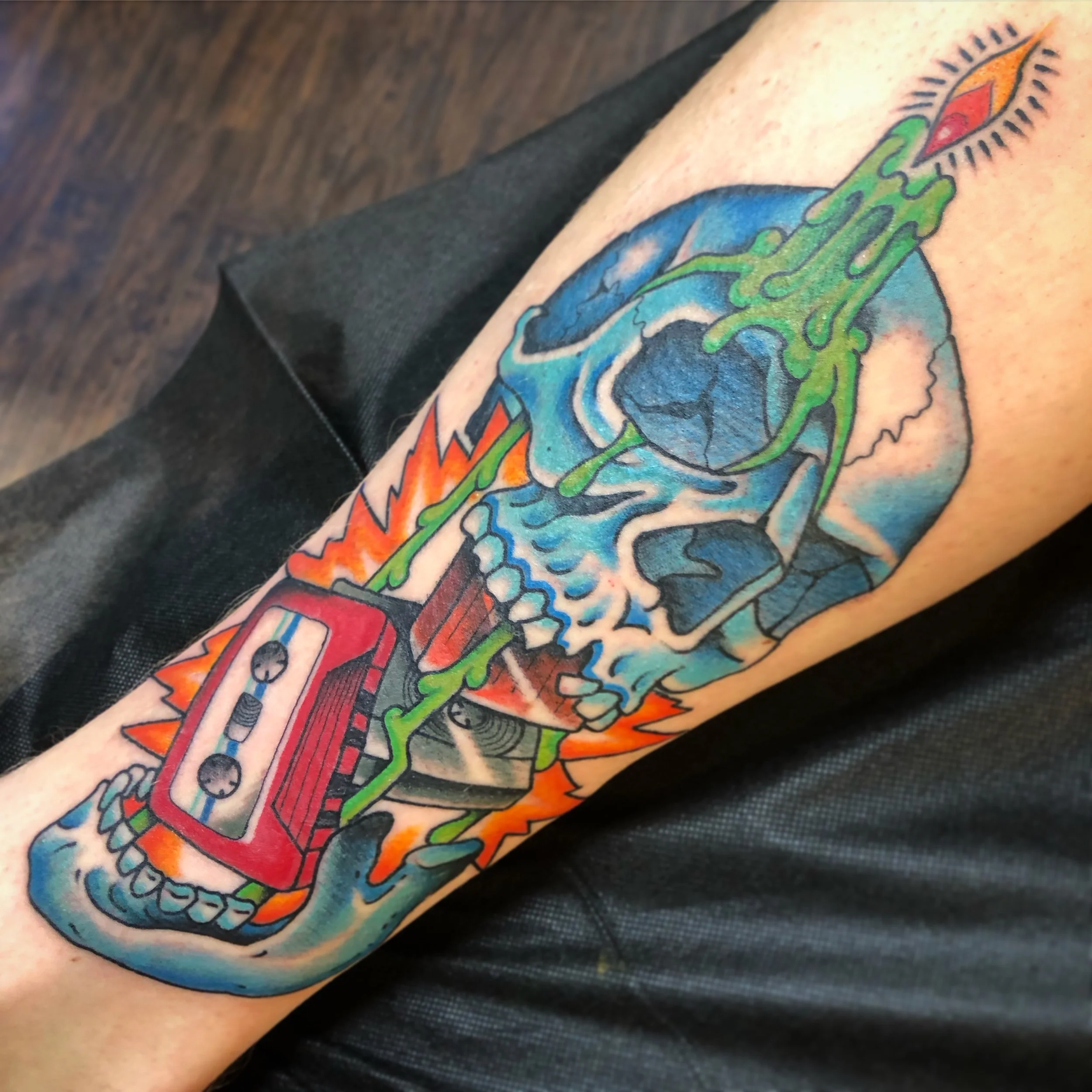 Colorful tattoo of a skull with a green candle, with a red cassette tape, with flame like burst background.