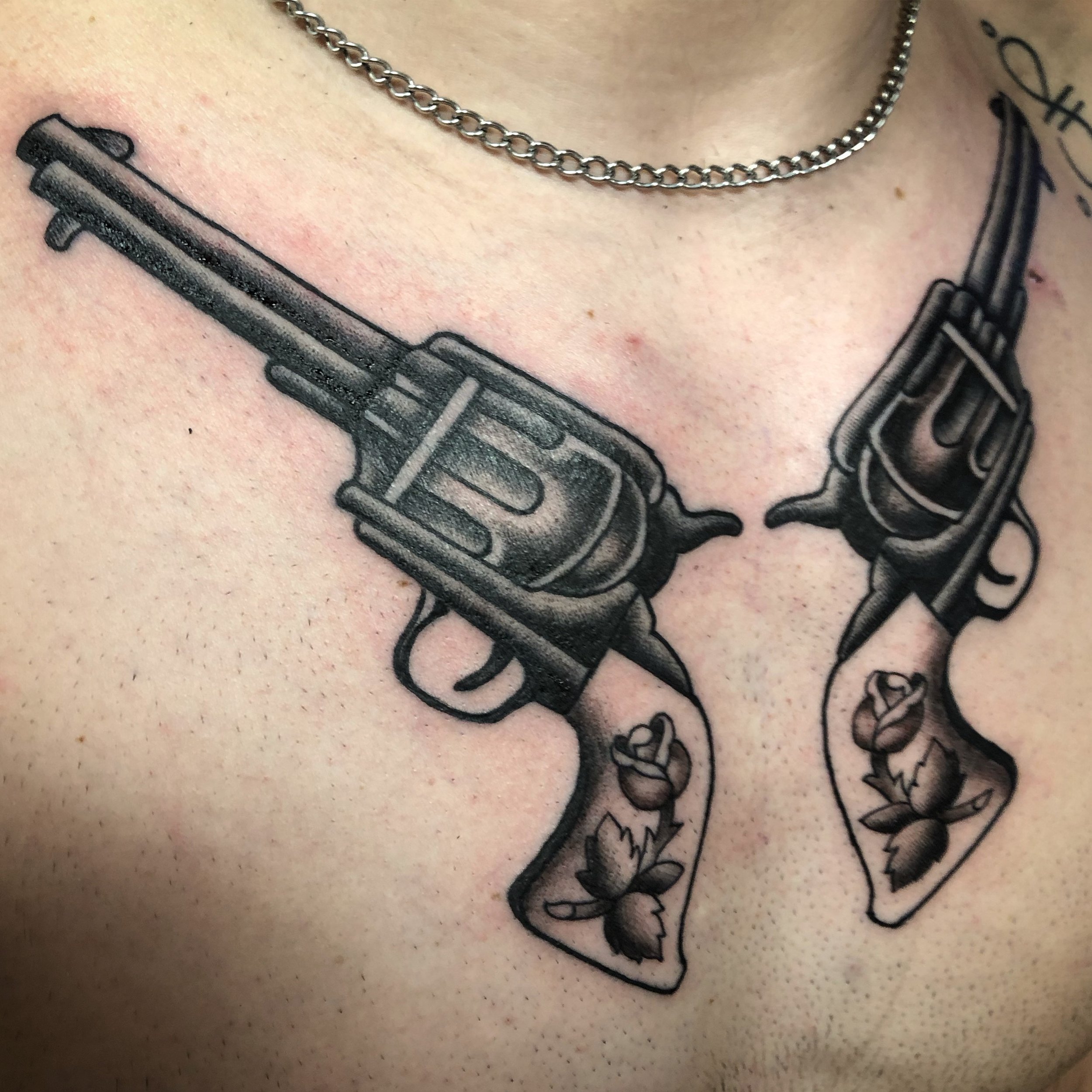 Tattoo of two revolvers crossed, with floral designs on the handles, on person's chest.