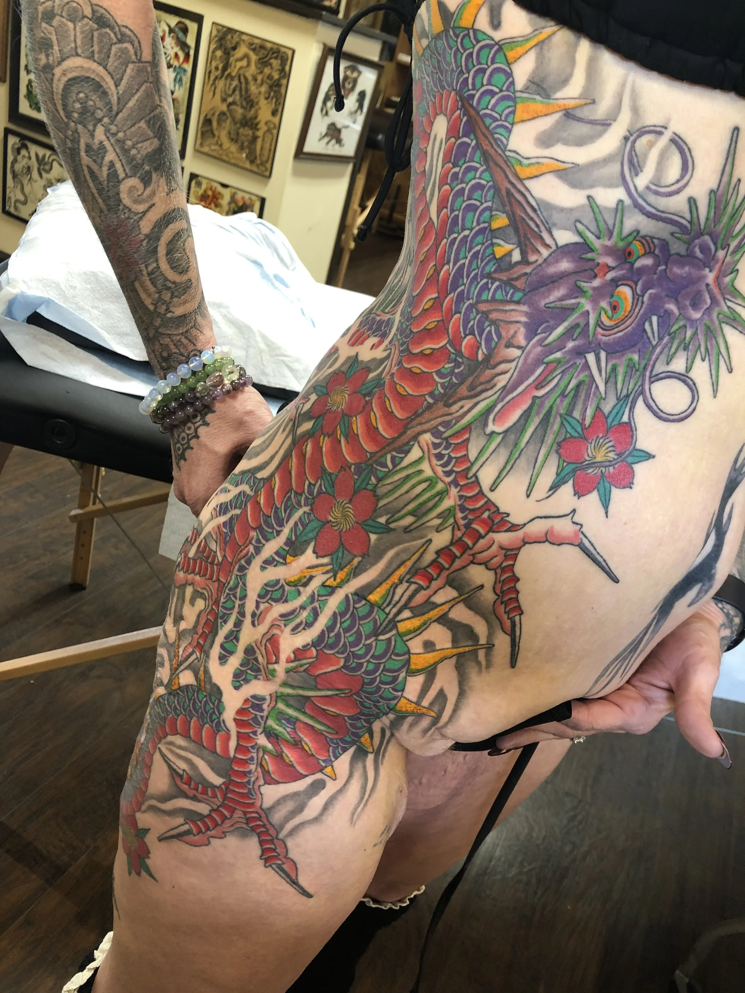 A person with an extensive tattoo of a dragon and cherry blossom extending from their torso to the lower leg
