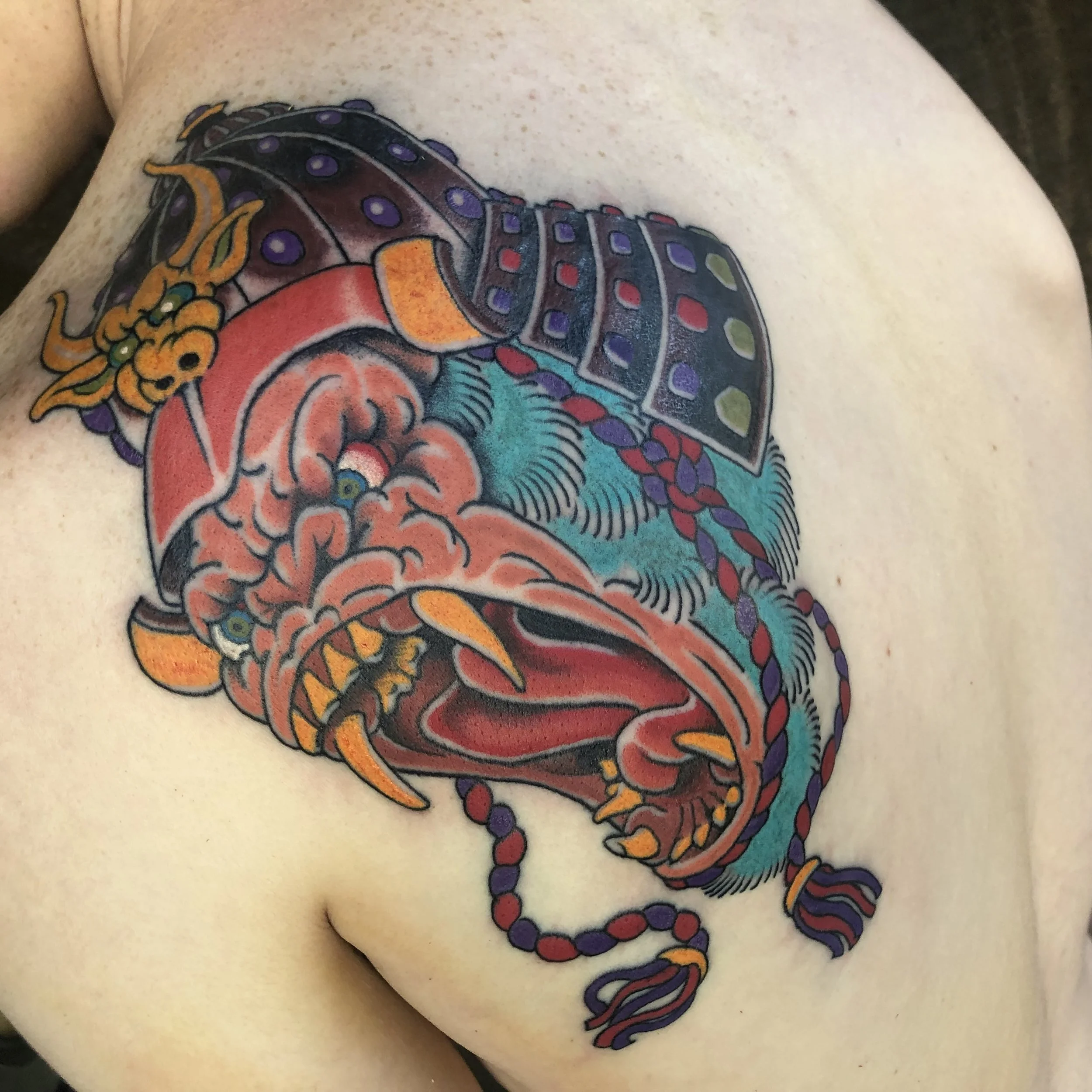 Colorful tattoo of a fierce, stylized dragon's head on a person's shoulder.