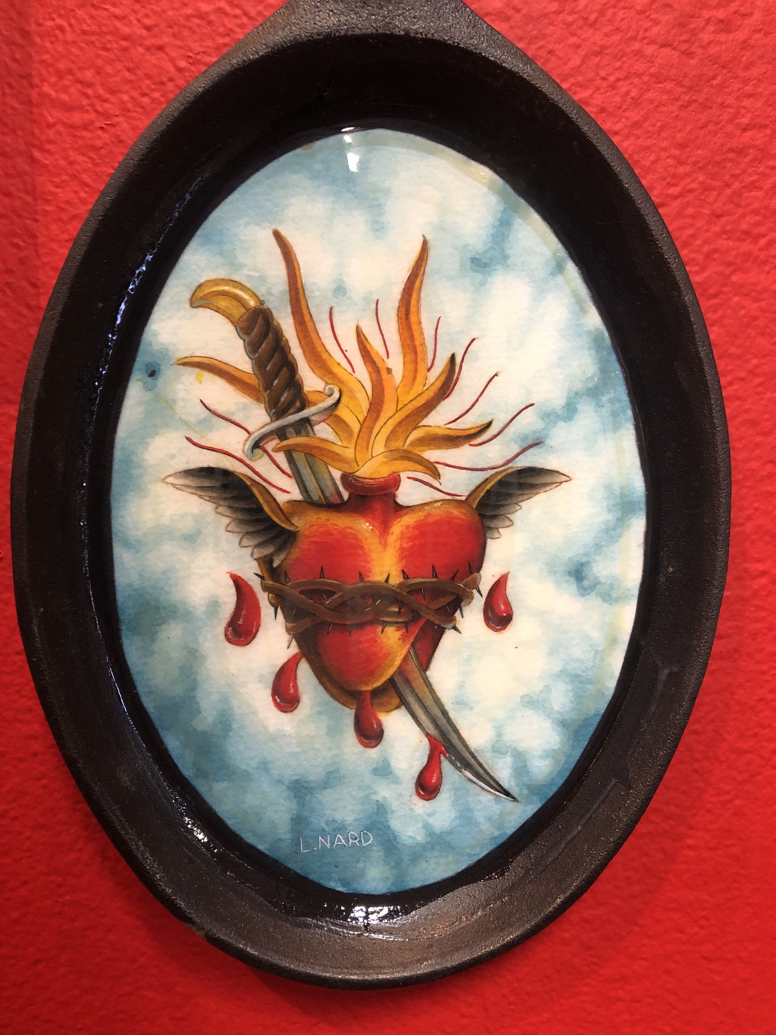 Tattooed heart with wings, barbed wire, and a dagger through it, against a blue sky background.