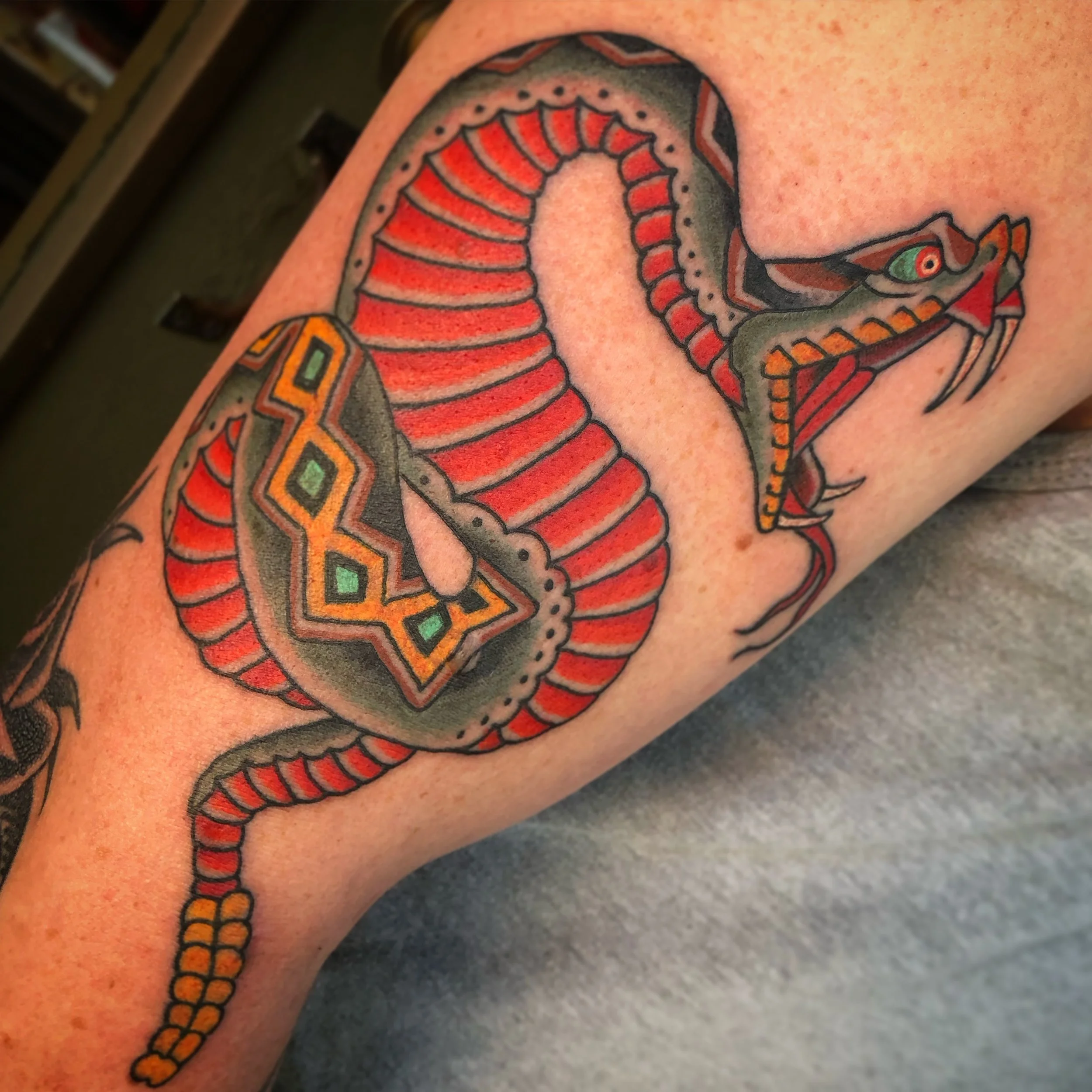 Tattoo of a stylized, traditional snake with red and black accents on a person's arm.