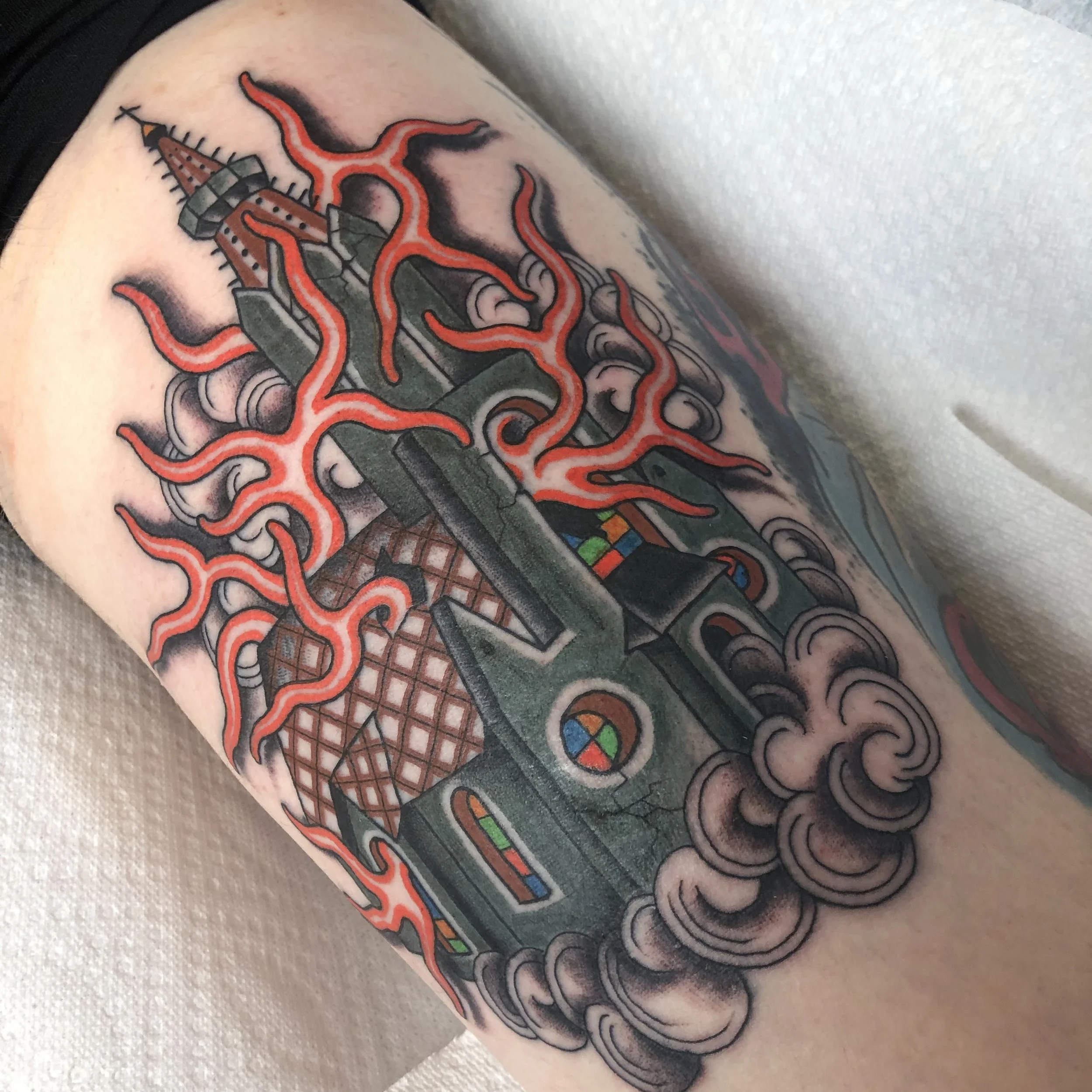 Tattoo of a gothic church emitting red flames and surrounded by dark clouds on the thigh
