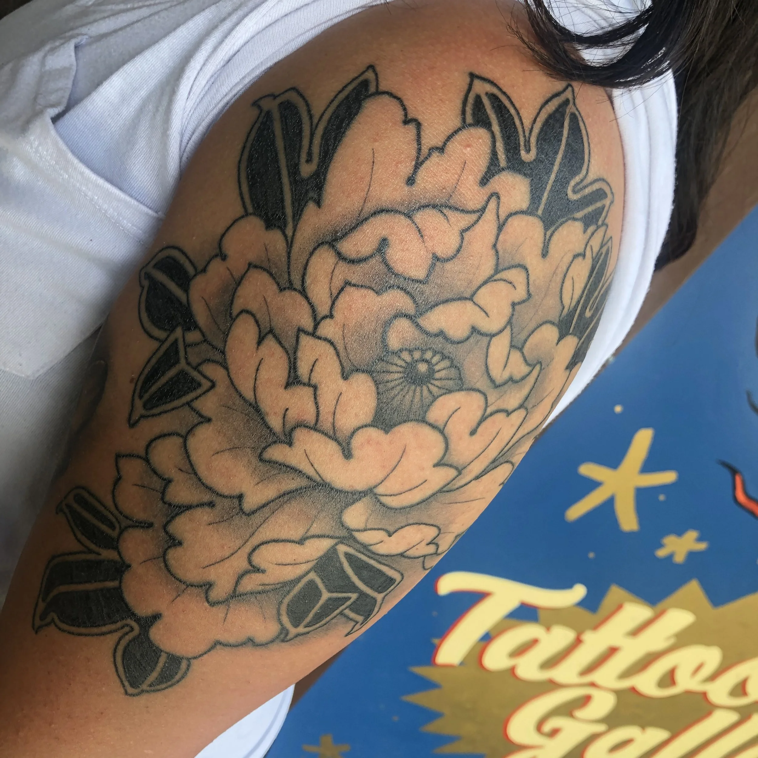Tattoo of a stylized peony flower on person's upper arm.