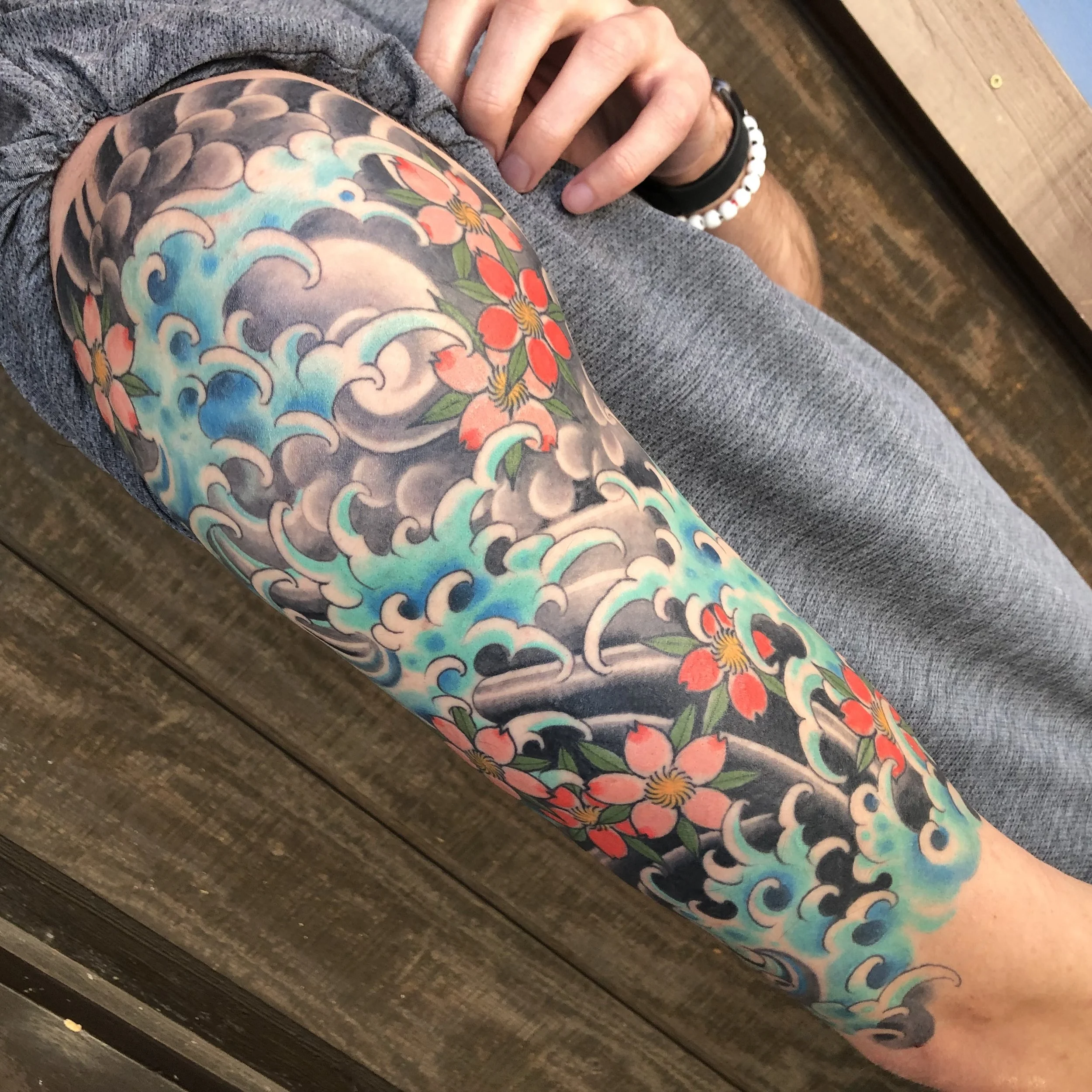 A person's arm with a colorful tattoo of waves and pink flowers.