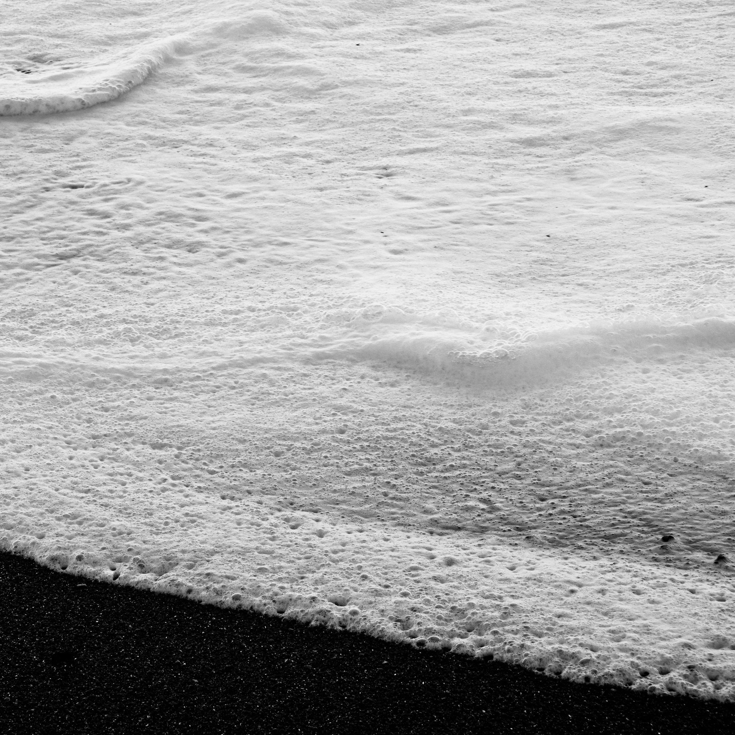 Vagues s'écrasant sur une plage de sable noir en noir et blanc.