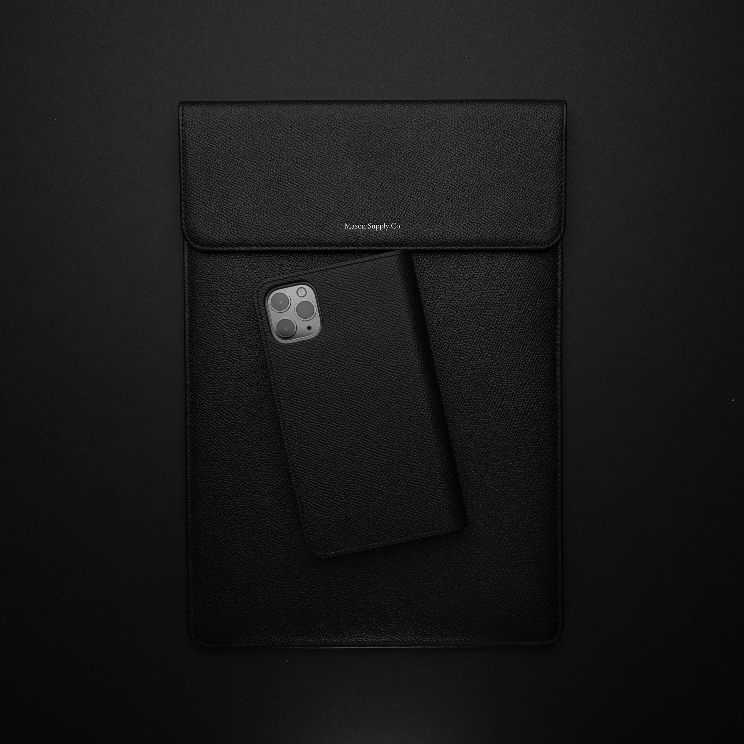 Un téléphone portable noir avec un étui en cuir, posé sur un grand carnet noir, le tout sur fond noir.