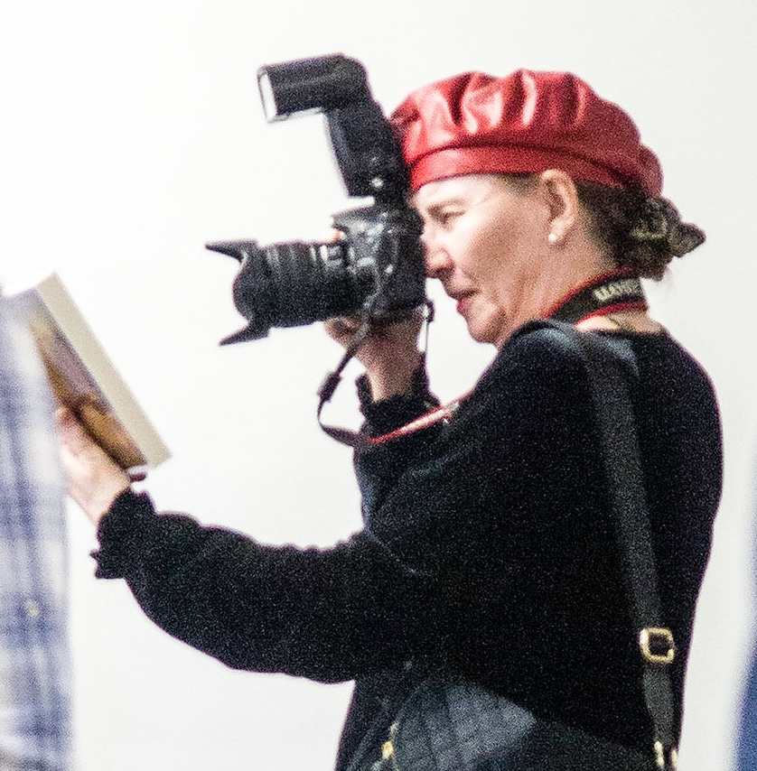 Woman wearing a red beret taking a photograph with a professional camera, reading a book.