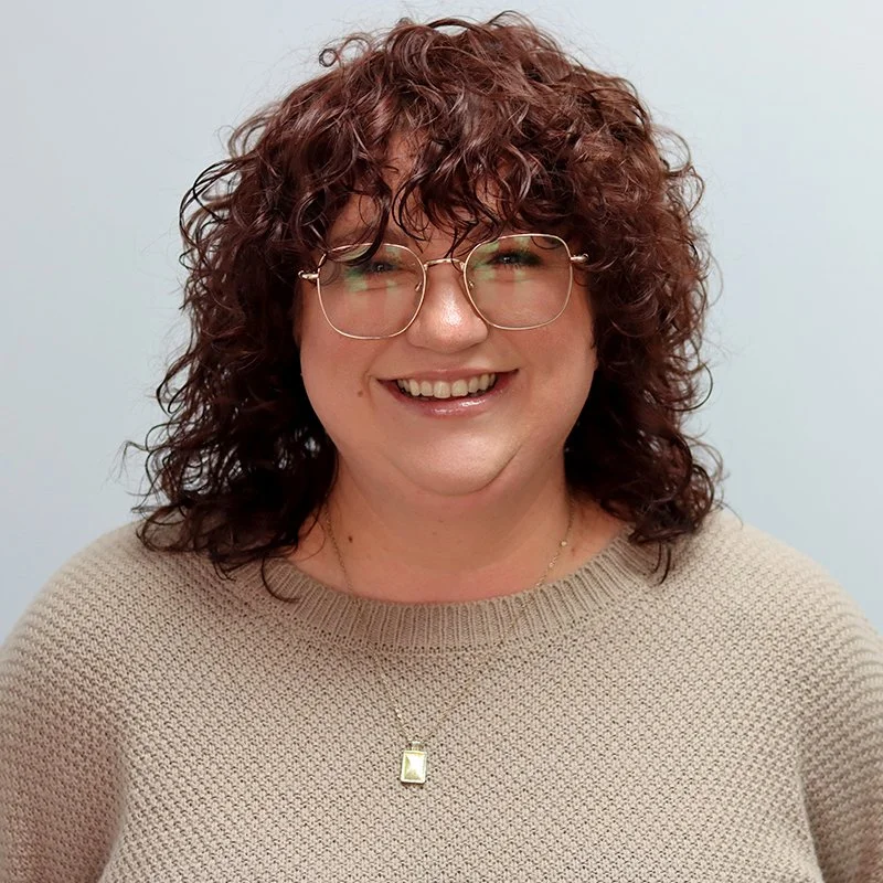 A young woman with dark hair styled in a messy bun, smiling and wearing a white top, against a plain white background.
