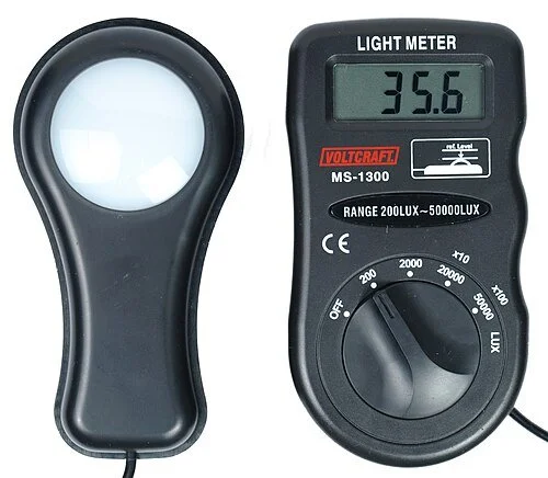 A digital light meter and a handheld magnifying glass on a white background.