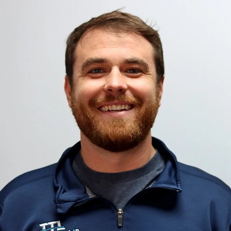 Young woman with dark hair styled in a messy bun, smiling, wearing a white top, against a plain white background.