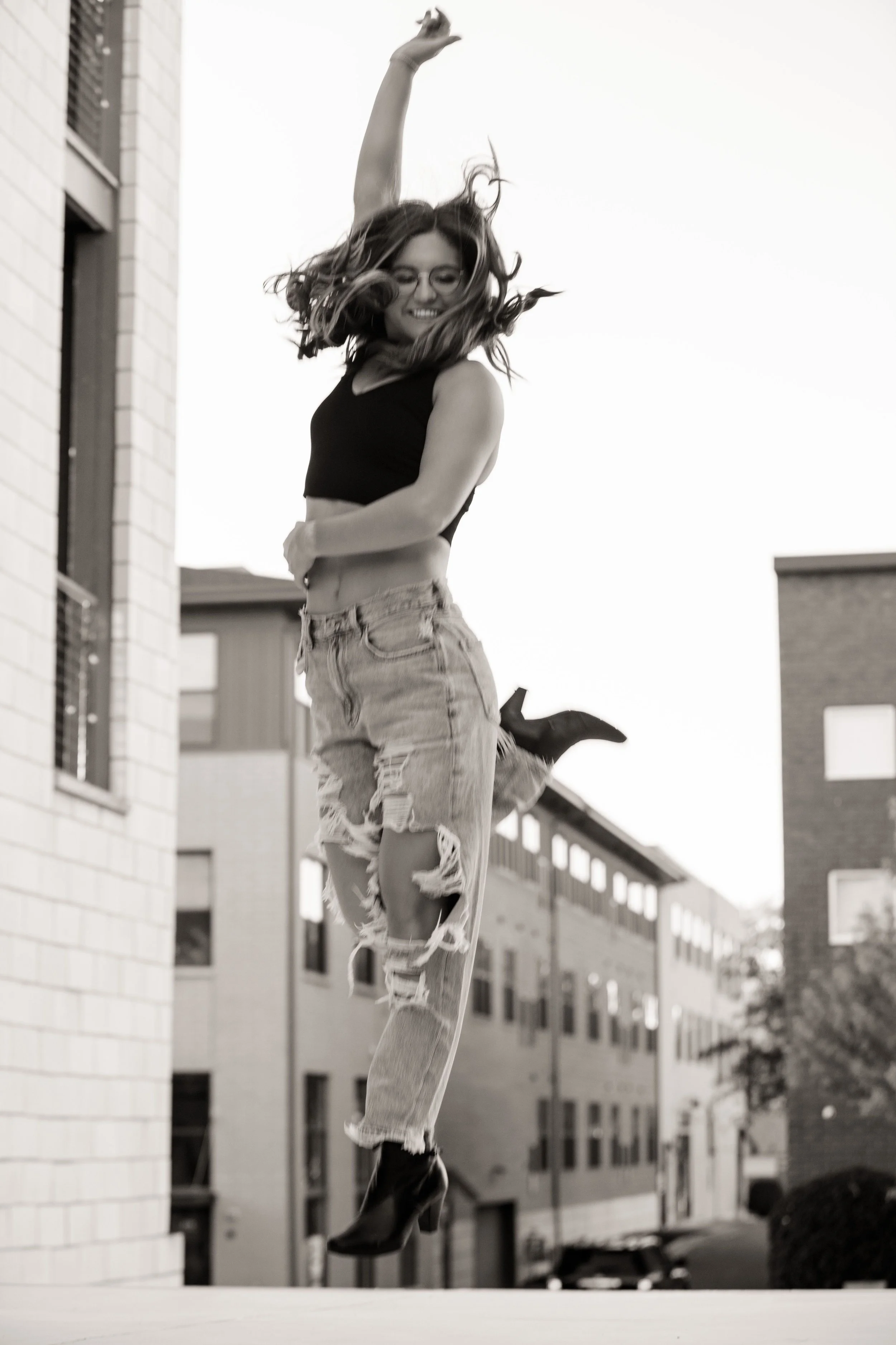 A high school senior lady jumping in the air outdoors in an urban area