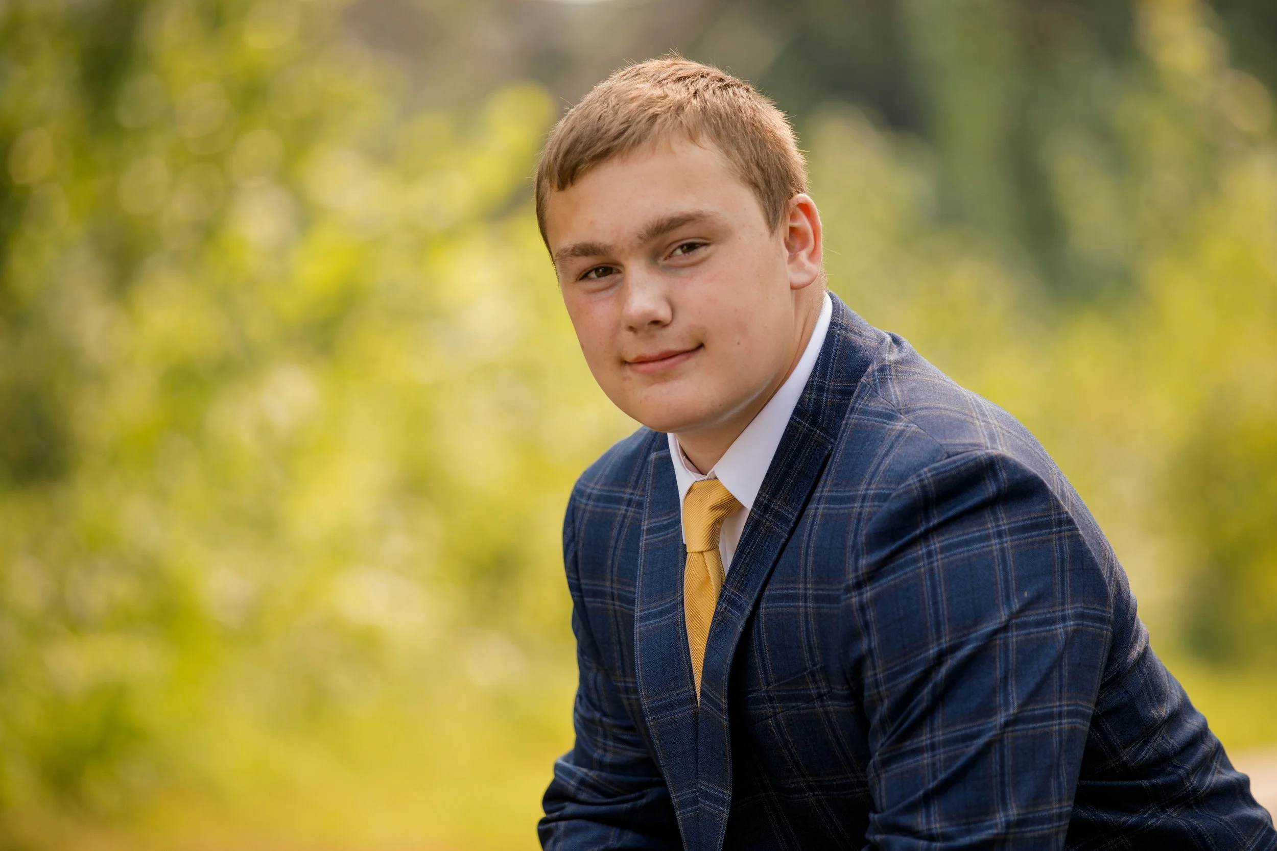 high school senior guy in a plaid suit coat with yellow tie and green trees in the background