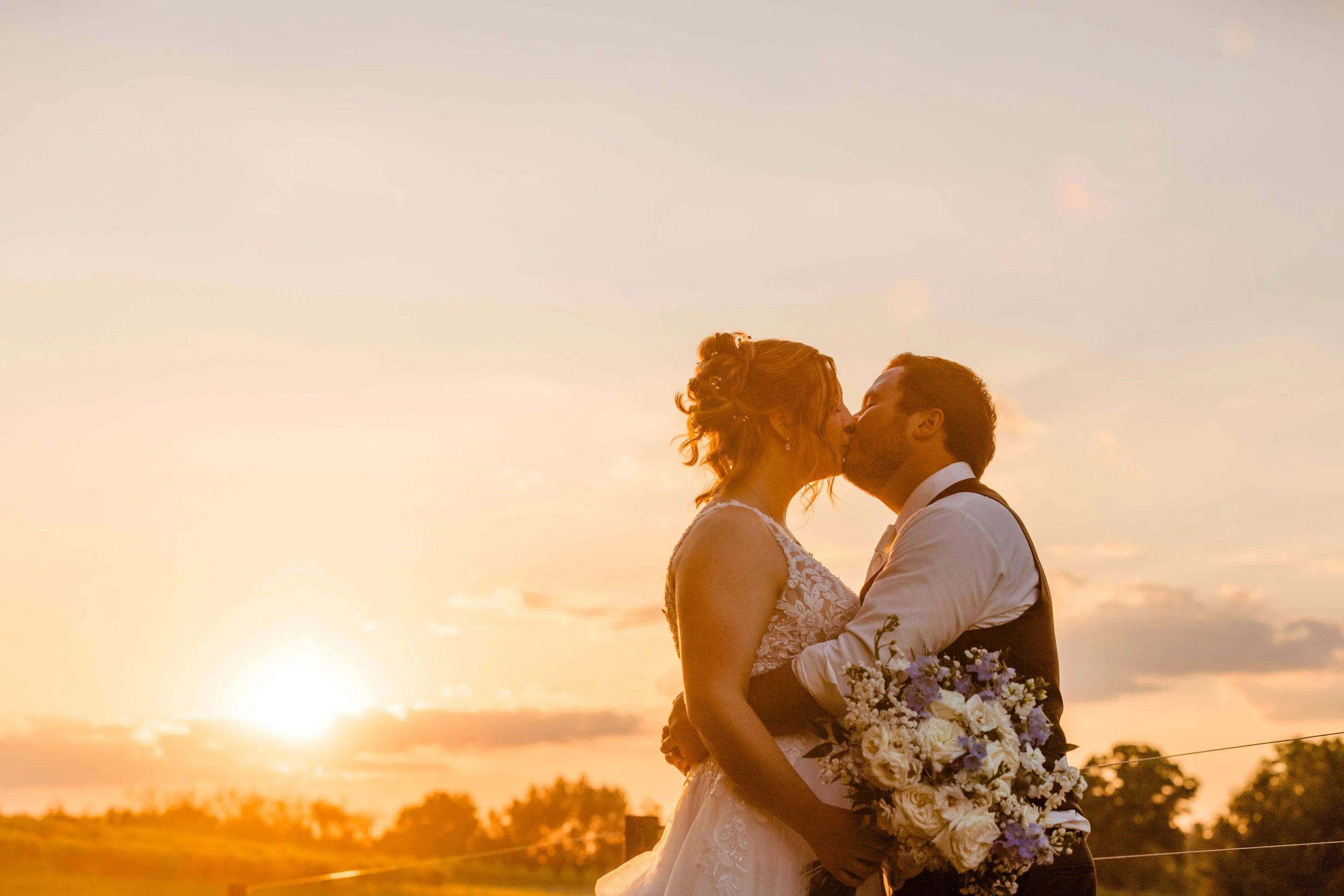 bride and groom kissing on the lips with a beautiful warm toned sunset