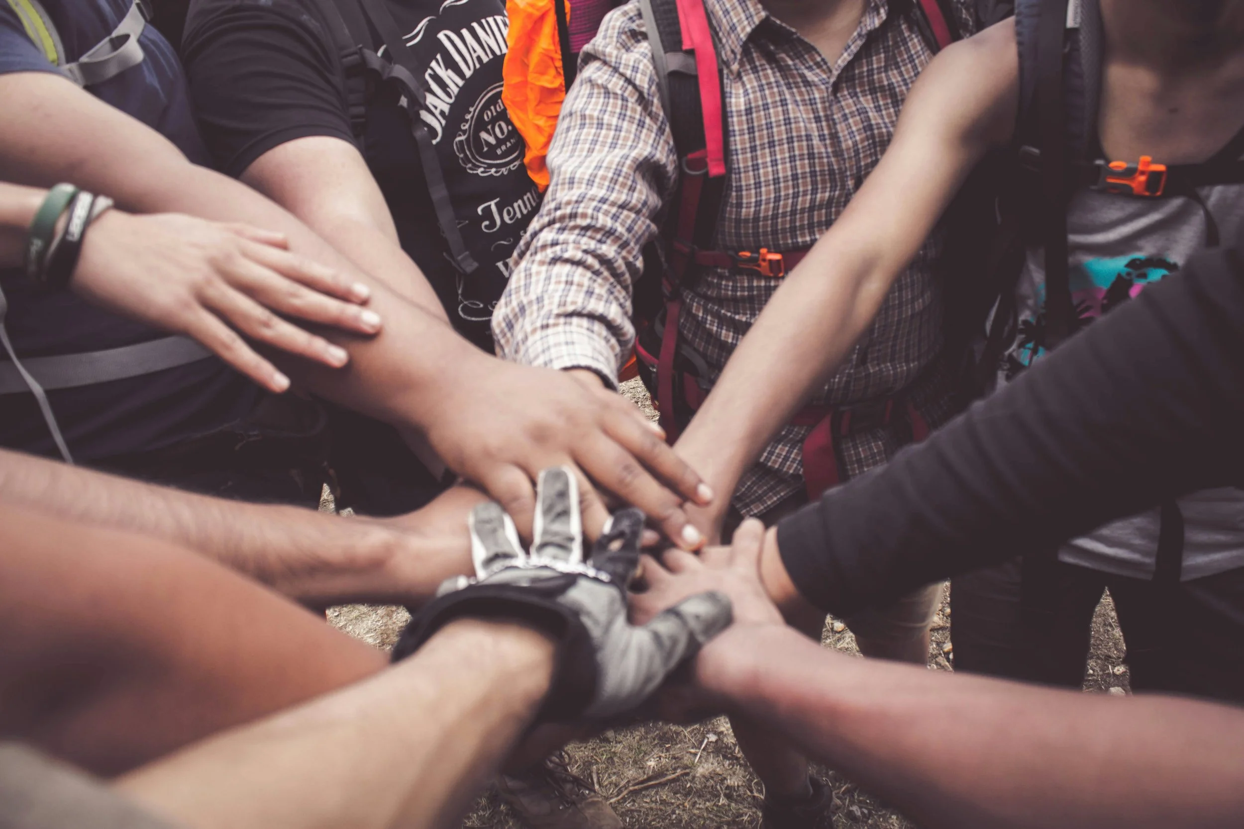 Group of people putting their hands together in a teamwork gesture outdoors.