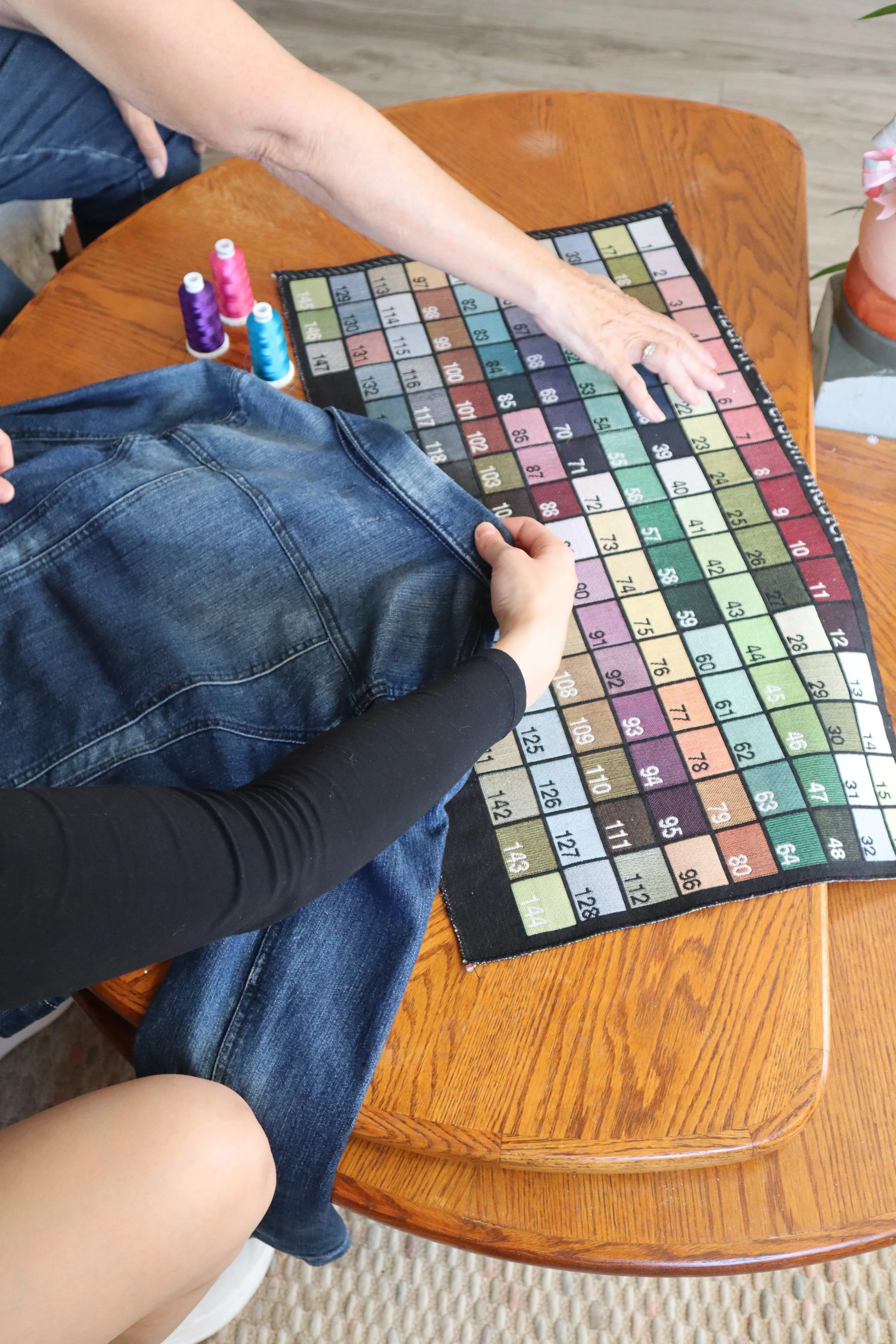 Close-up of a person pointing at a color-coded game board on a wooden table, with spools of thread nearby.