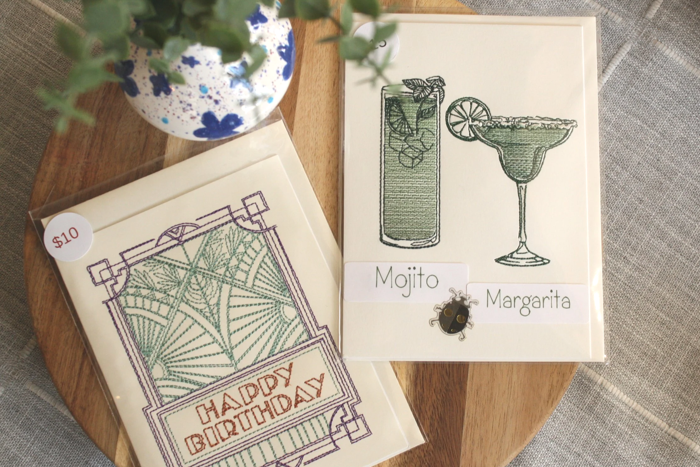 Coloring pages of cocktails and birthday message, a spray-painted decorated plate, and small cards with a $10 label on a wooden surface.