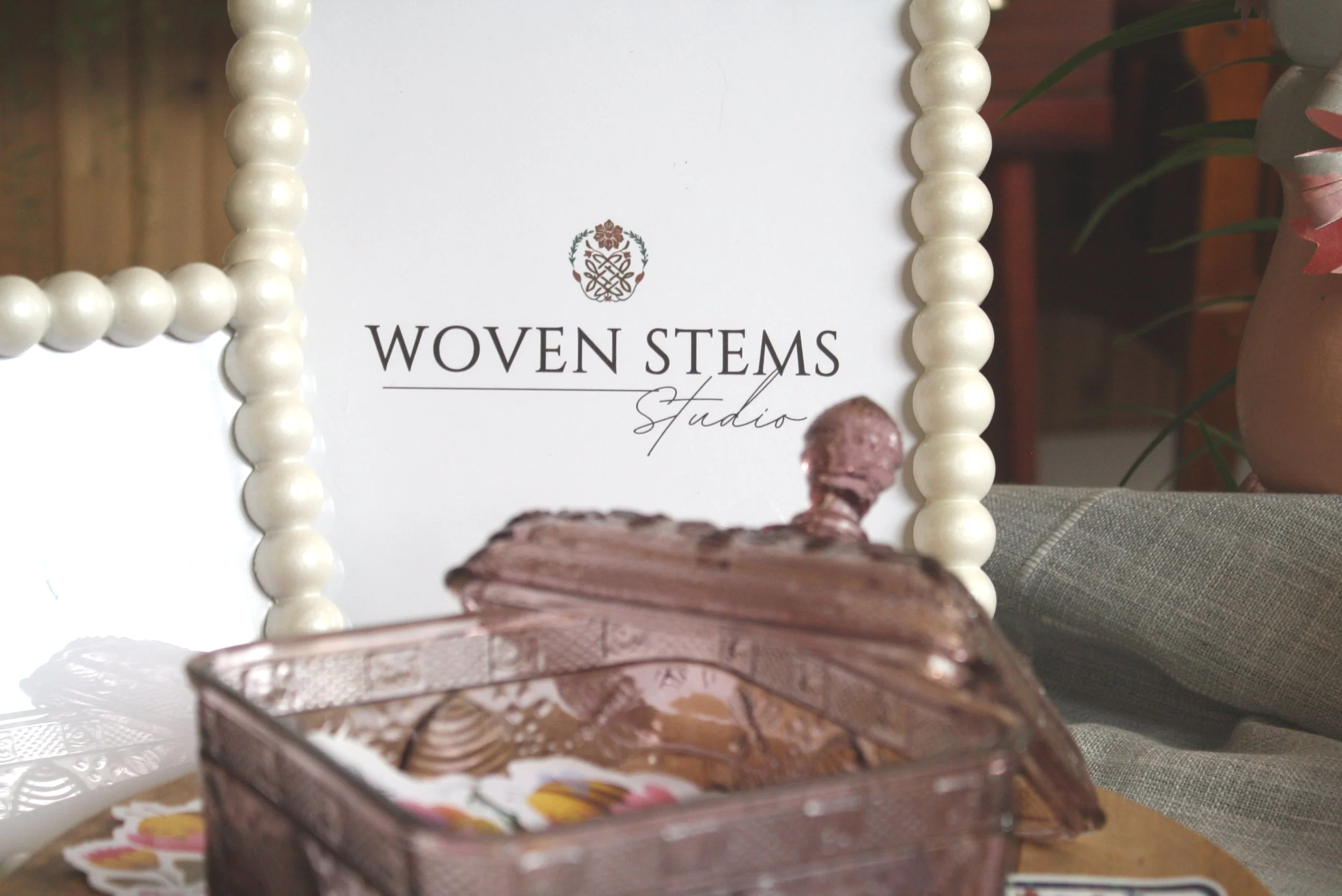 Chocolate layered cake with marbled frosting in a decorative box, in front of a sign that reads "Woven Stems Studio" with cream-colored beaded frame around the sign, on a table with stickers.
