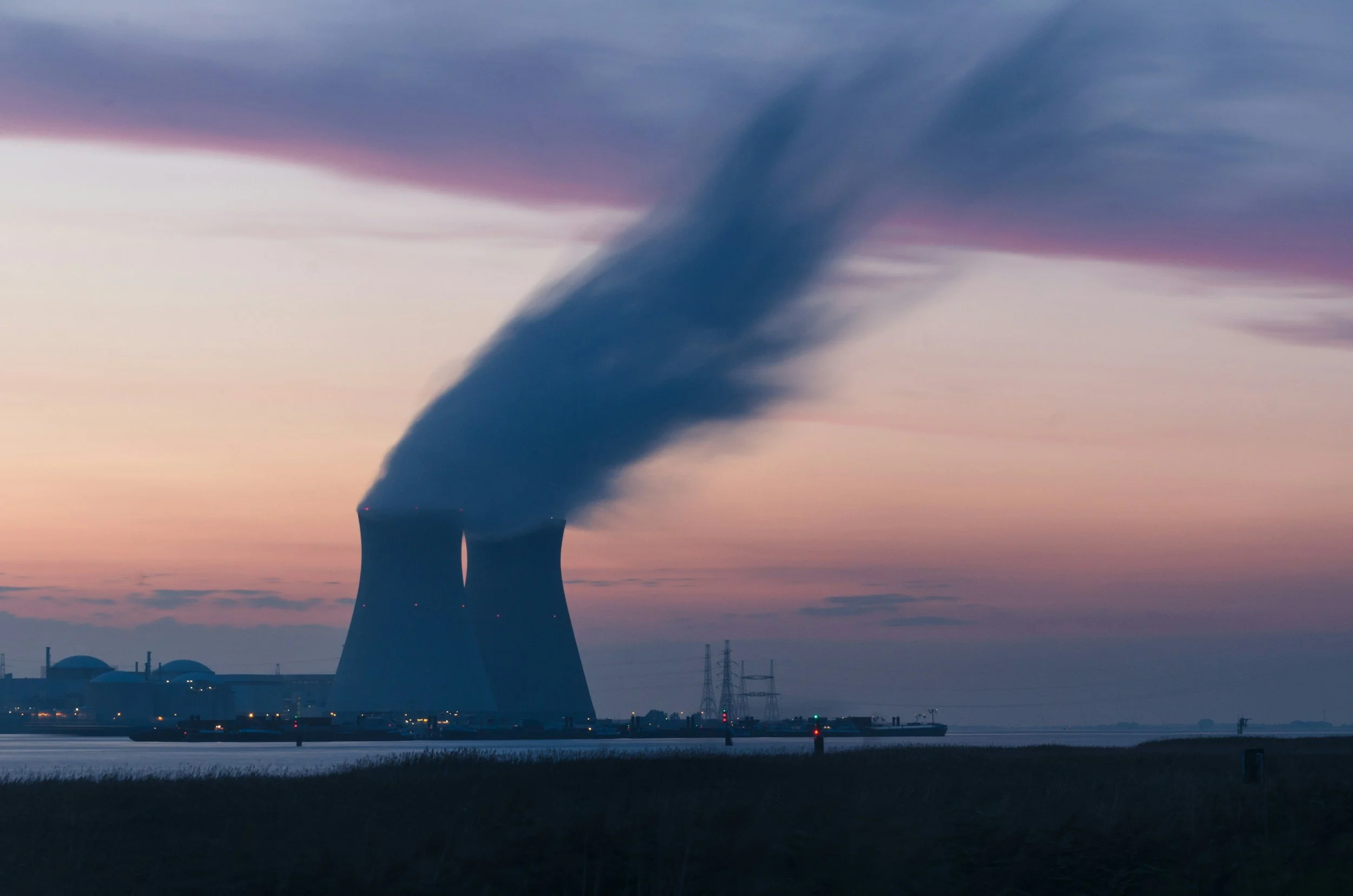 Nuclear power plant with cooling towers emitting steam at sunset.