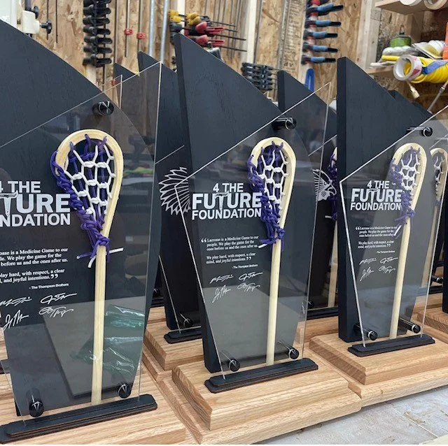Lacrosse stick trophies with clear glass plaques and the text "4 THE FUTURE FOUNDATION" at an awards ceremony or event.